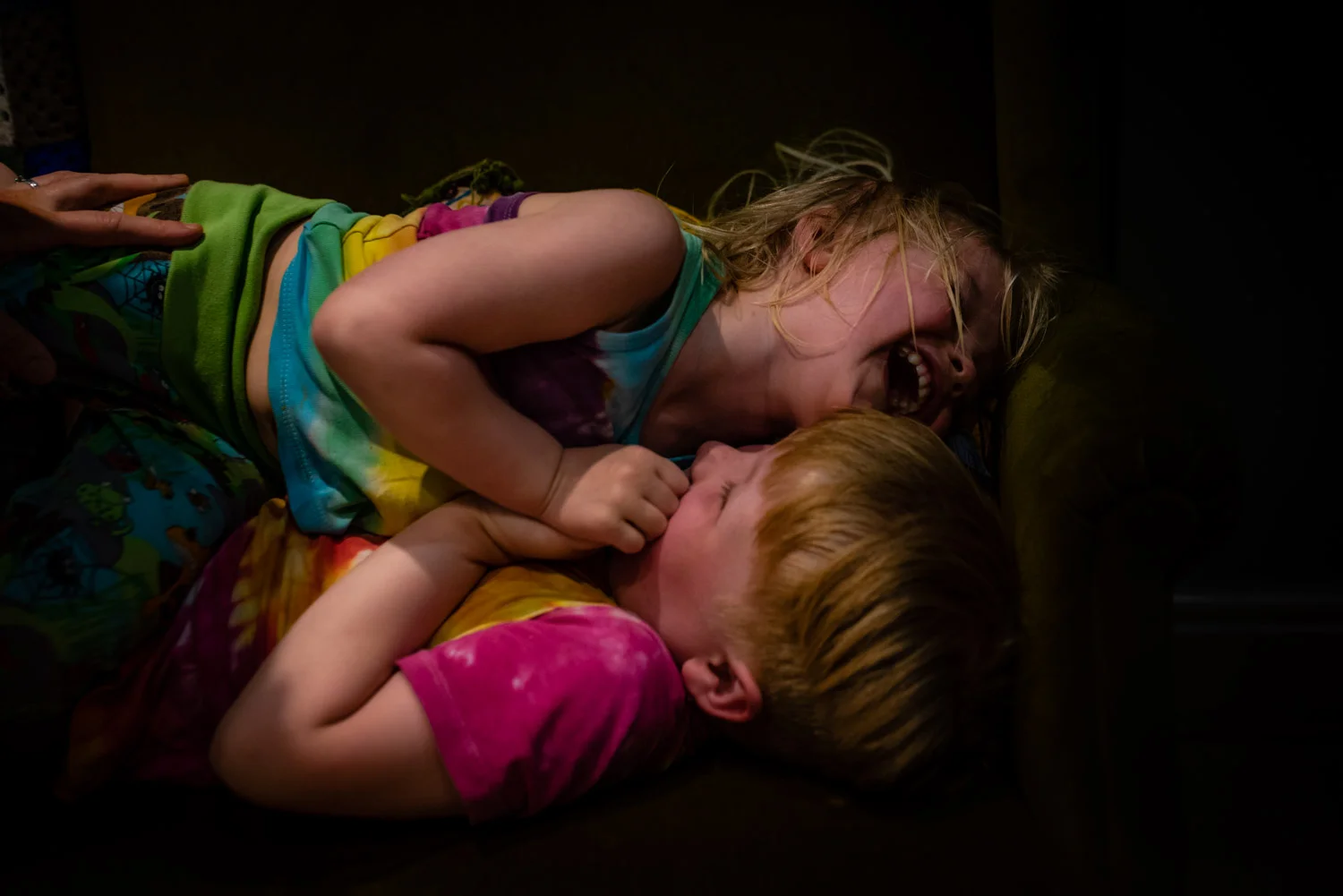 Two brothers lie on their sofa laughing together whilst they are being tickled during this relaxed, unposed, family photo shoot.