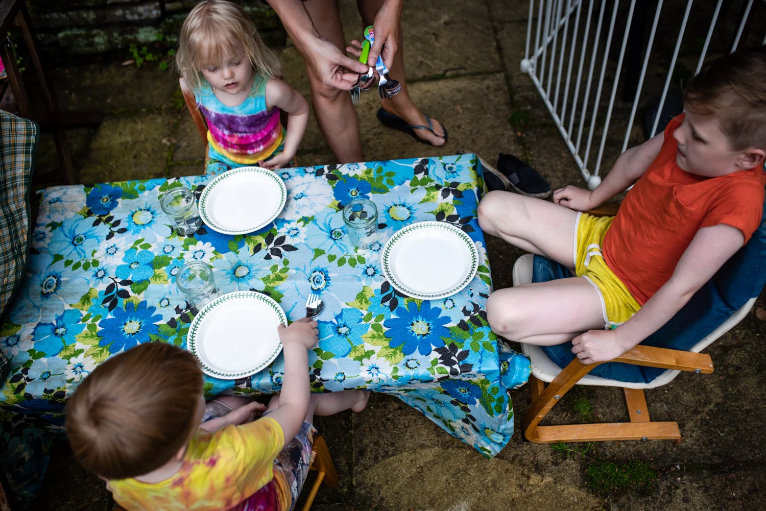Three brothers sit at their table waiting for their dinner as their mother lays their cutlery down during this family portrait photo session.