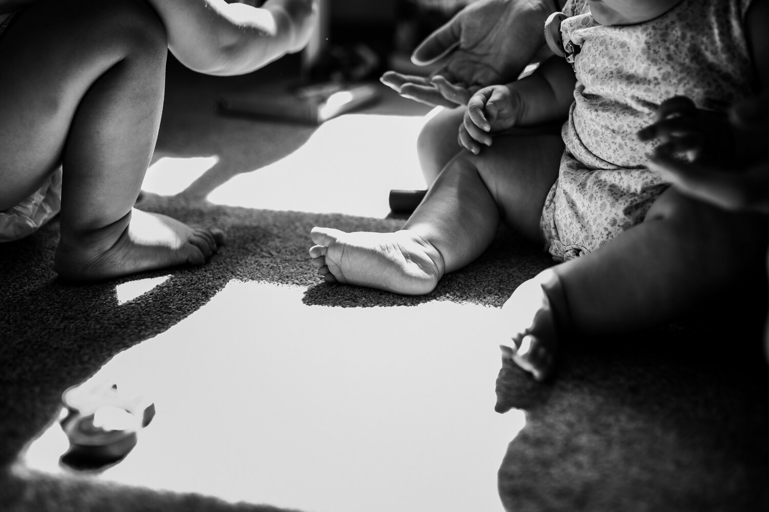  A close up shot of a childrens and mothers feet in black and white with light dappling through the middle. 