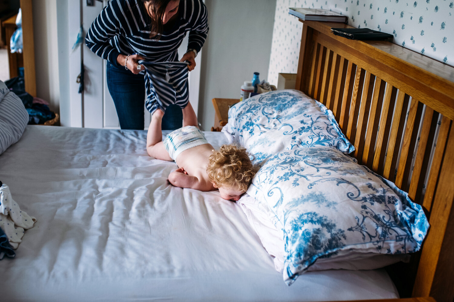  Mother playfully wrestling son on the bed while trying to get him dressed during in-home photo session in Bath. 
