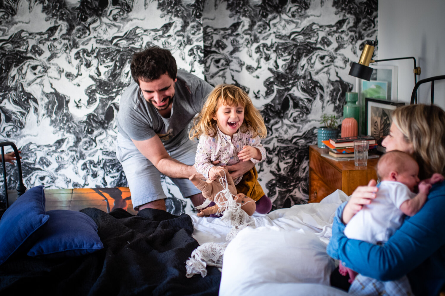  A father throws his daughter onto the bed playfully as her mother who is cradling her newborn looks on adoringly during this family photo shoot in Bath. 