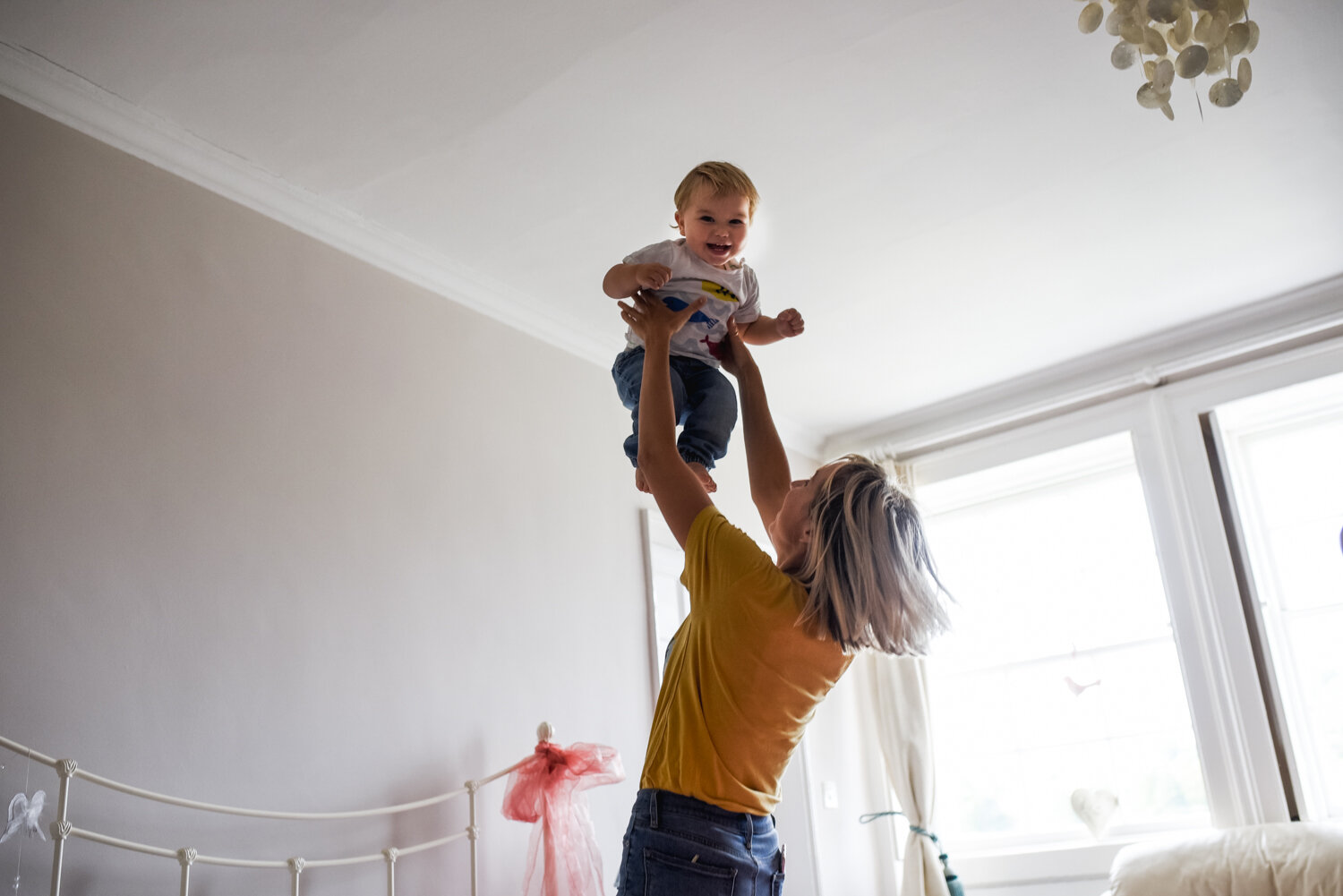  A mother throws her baby up into the air in her bedroom and the baby laughs joyfully during this at-home family session in Bath, Somerset. 