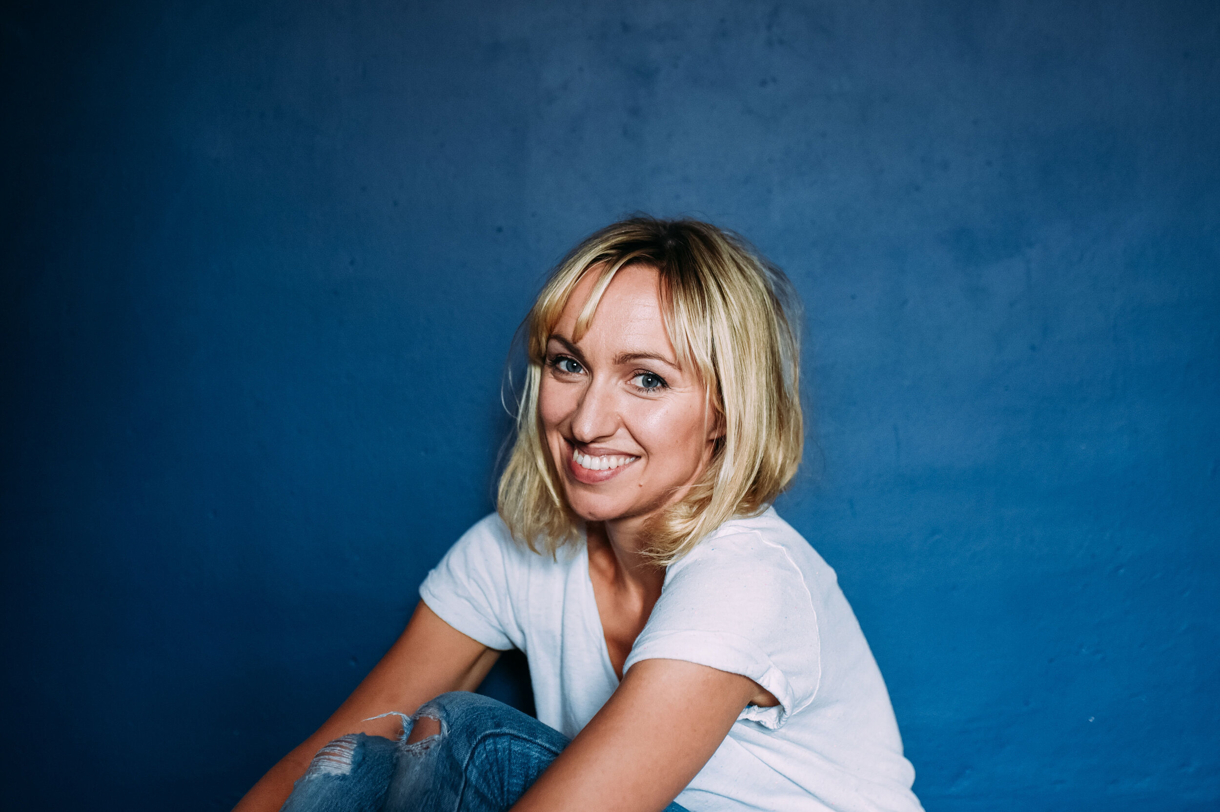  An actress sits in front of a blue wall smiling during this portrait photography session for actor headshots in Bath Somerset. 