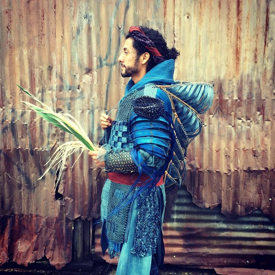Igor Santizo as Chronos in a garment made from yucca, abaca (a species of banana), silk and dyed willow bark. He holds a sheaf of stripped yucca leaves. He is armed against the sun with expanding screens protecting the head and spine, sheathed leaf sleeves that shade and let breeze through.