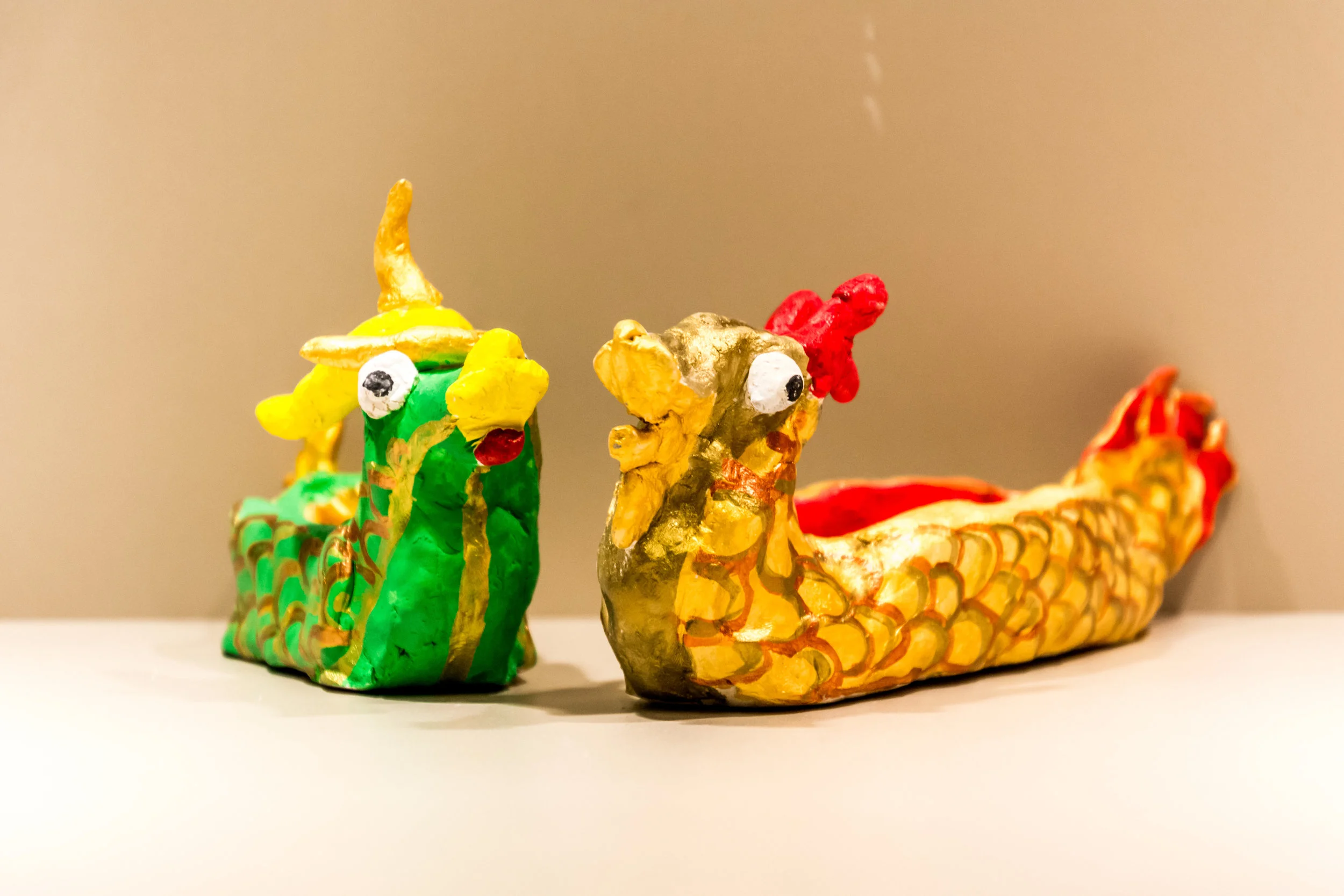 Photo Description: Two dragon boats with a green on with gold trimming one the left and a gold with red trimming one on the right.