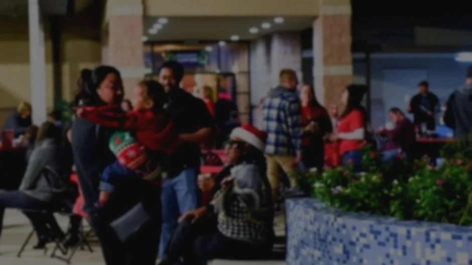 People celebrating Christmas at an indoor event, some wearing Santa hats, in a decorated area with a Christmas tree and festive decorations.