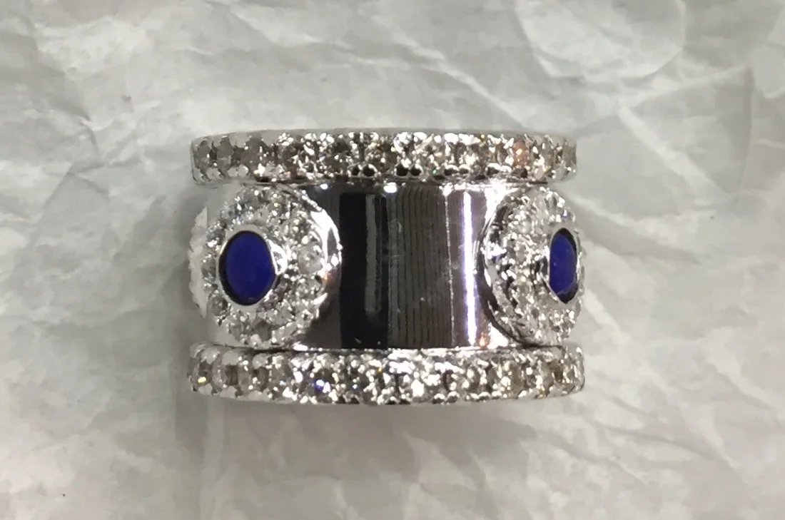 WiDE WHITE GOLD BAND WITH DIAMOND EDGES AND ENHANCED BY LAPIS IN CIRCLED WITH DIAMONDS.