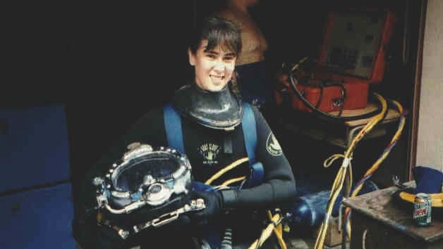 Dominique waits for the final phase of gear up before entering the diving well at Santa Barbara City College. Surface-to-diver communication equipment can be seen in the background (orange box). Tenders constantly monitor divers underwater using hardline communication.