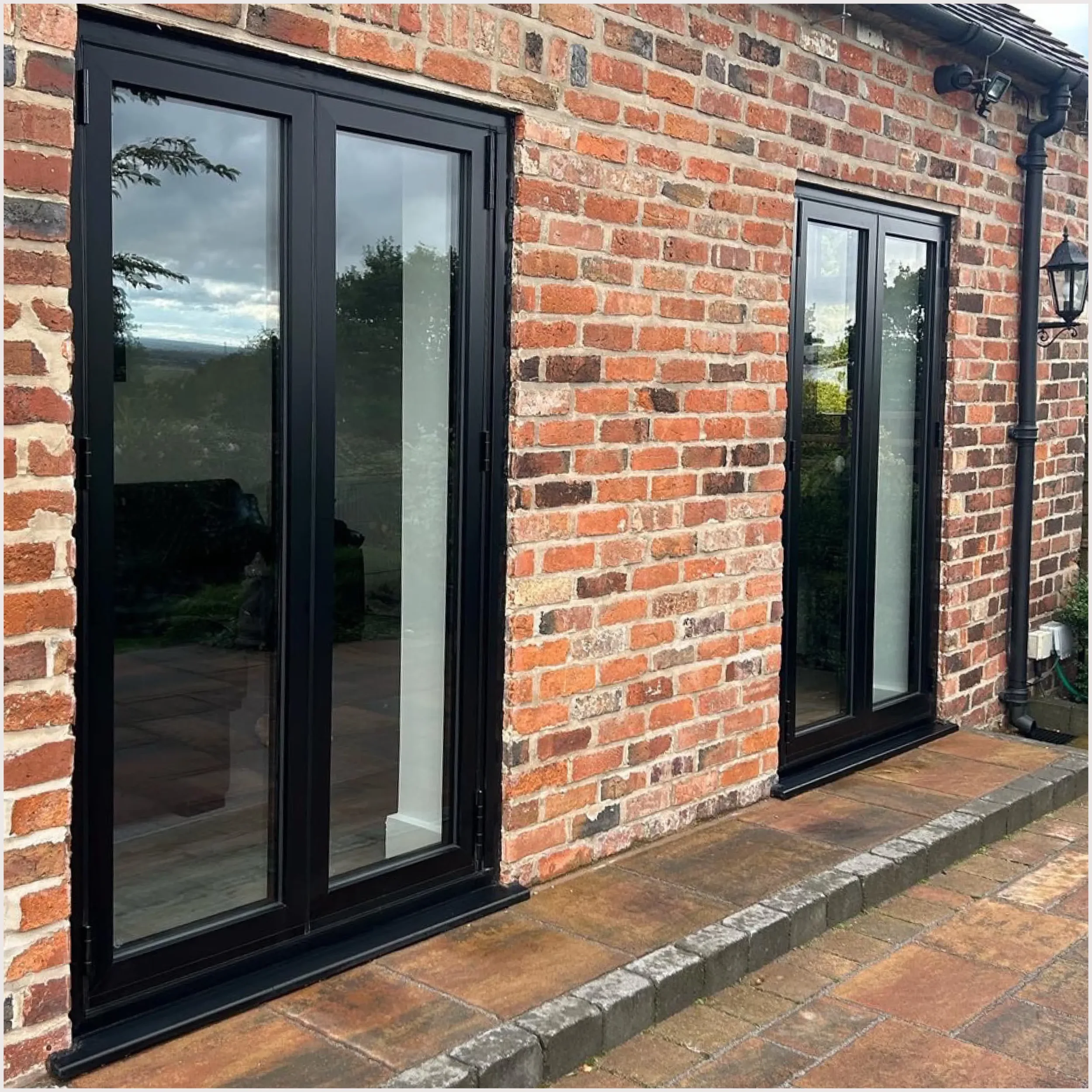 A brick house exterior with black-framed glass sliding doors and a metal lantern-style outdoor light fixture.