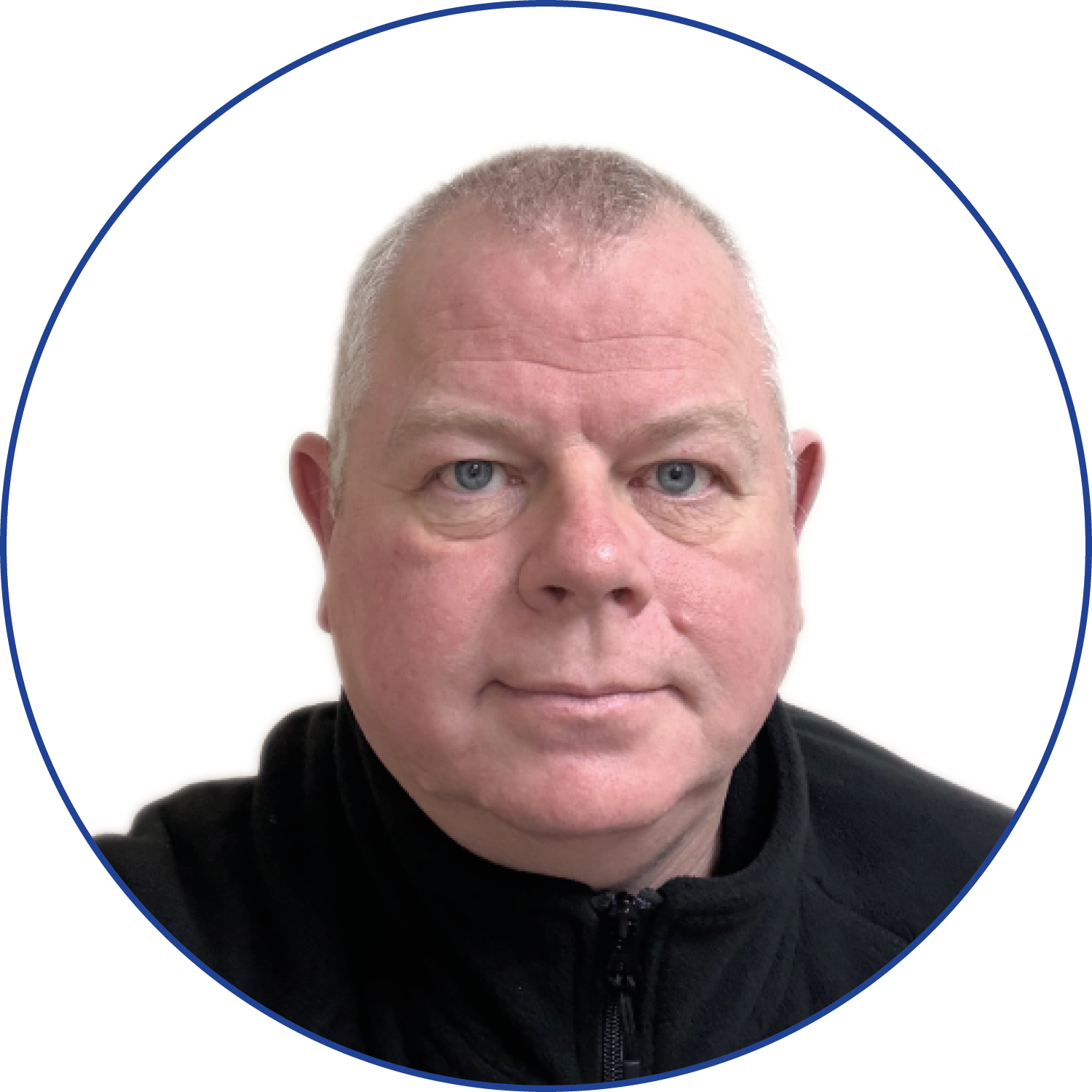 Close-up photo of a middle-aged man with short gray hair, blue eyes, and a serious expression, wearing a black zip-up jacket, against a plain white background with a blue circular border.