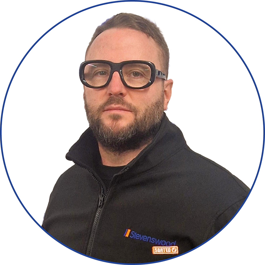 A man with a beard and glasses wearing a black jacket with a 'Stevenswood' logo and a 'SORTEO' patch, posing against a white background with a blue border.