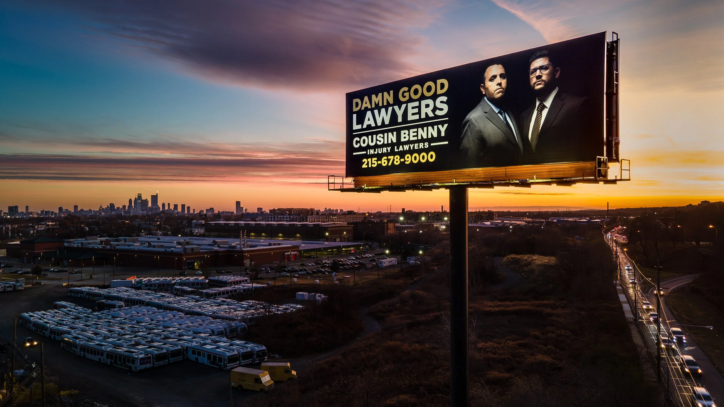 Billboard advertising a law firm featuring two men in suits, with a city skyline and sunset in the background.