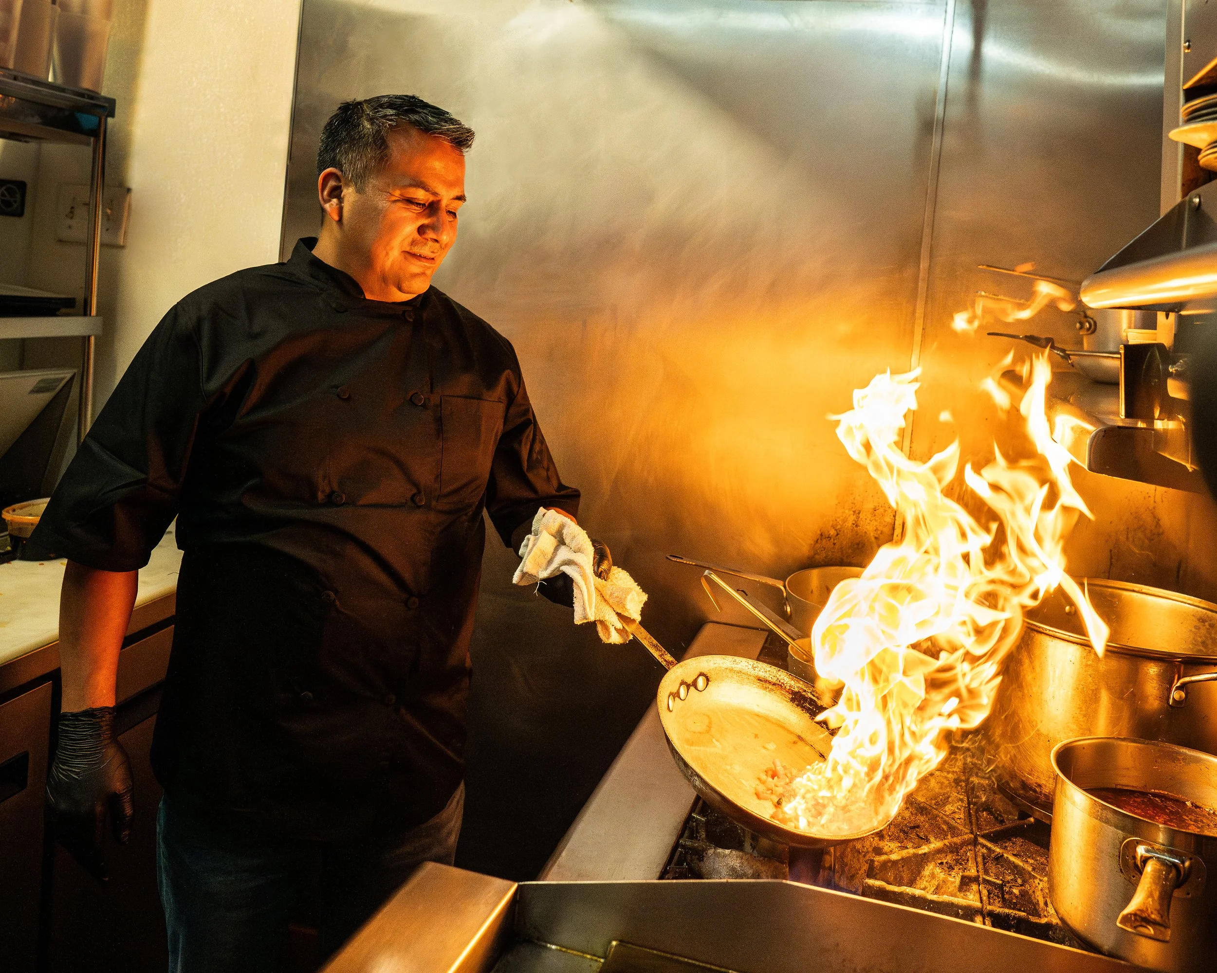 A chef in a black uniform cooking with a large flame in a professional kitchen.