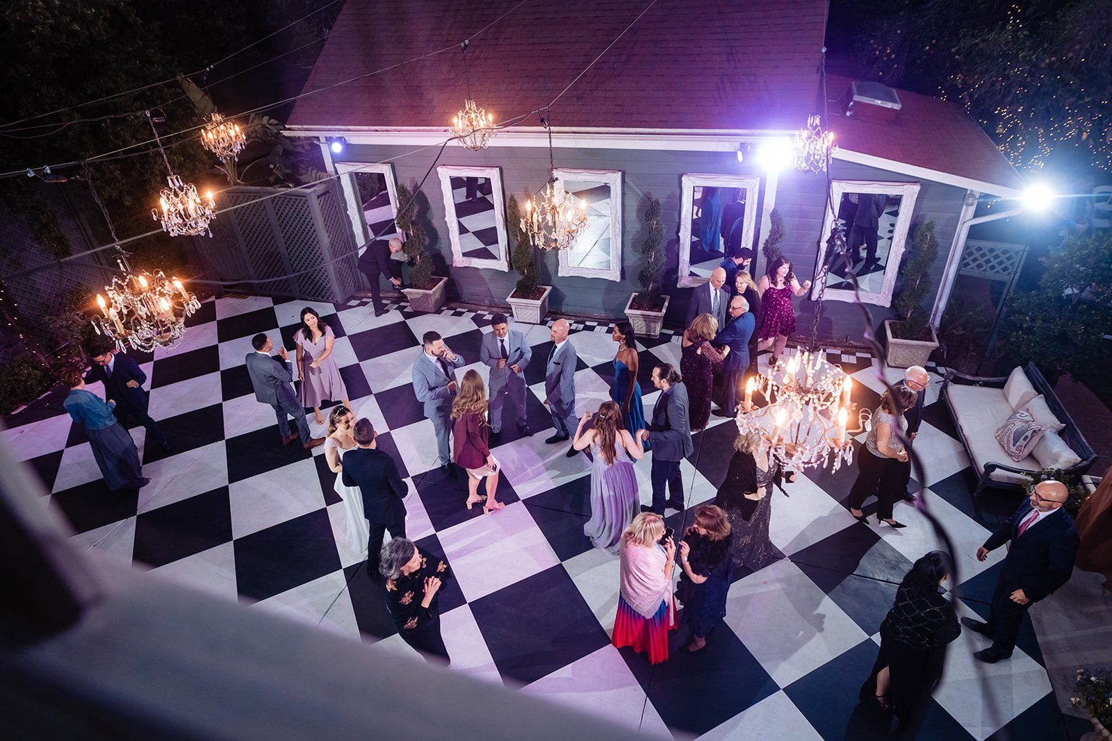 a black and white checkered dance floor full of guests dancing at an outdoor wedding reception