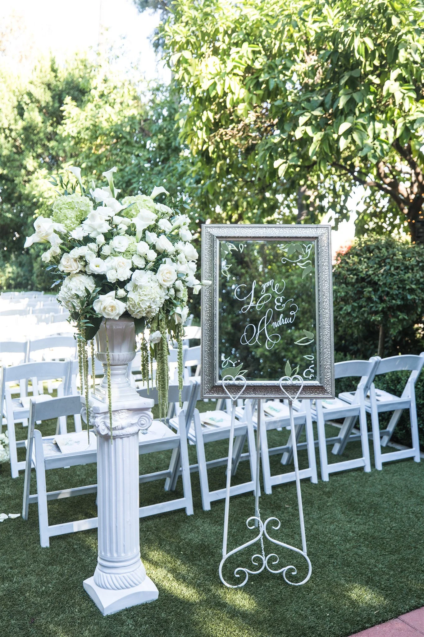 Wedding welcome sign at the ceremony entrance with classic white floral arrangements and white ceremony chairs