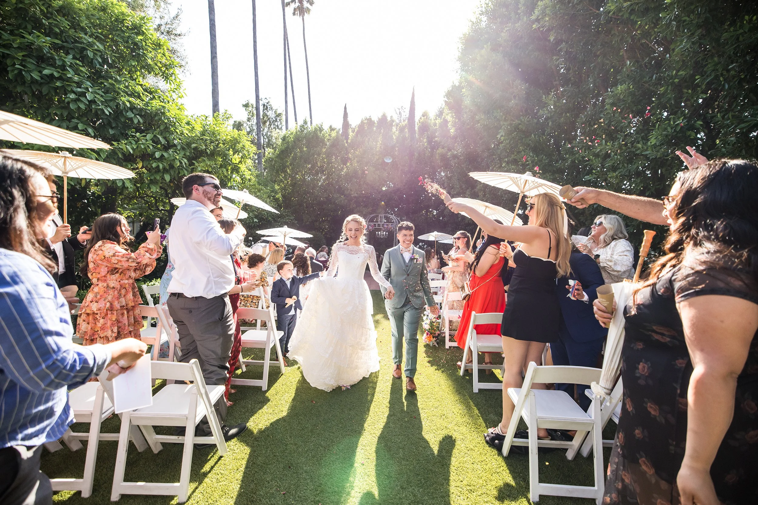 Happy couple walking down the aisle during their wedding recessional as guests toss dried flower petals in the White Garden