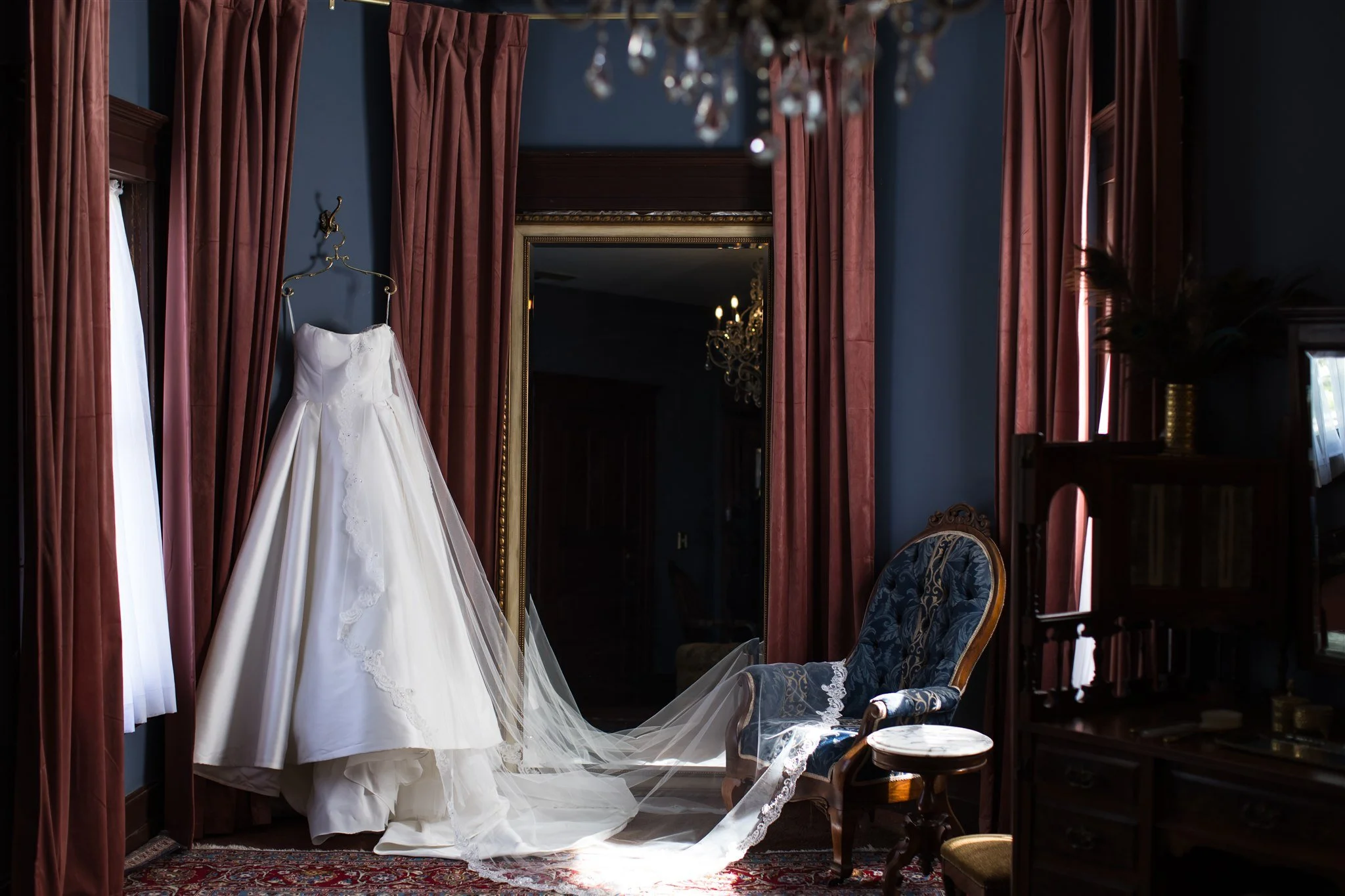 Bride’s wedding dress hanging beside a gilded mirror in the Celebration Suite dressing room at a historic Southern California wedding venue