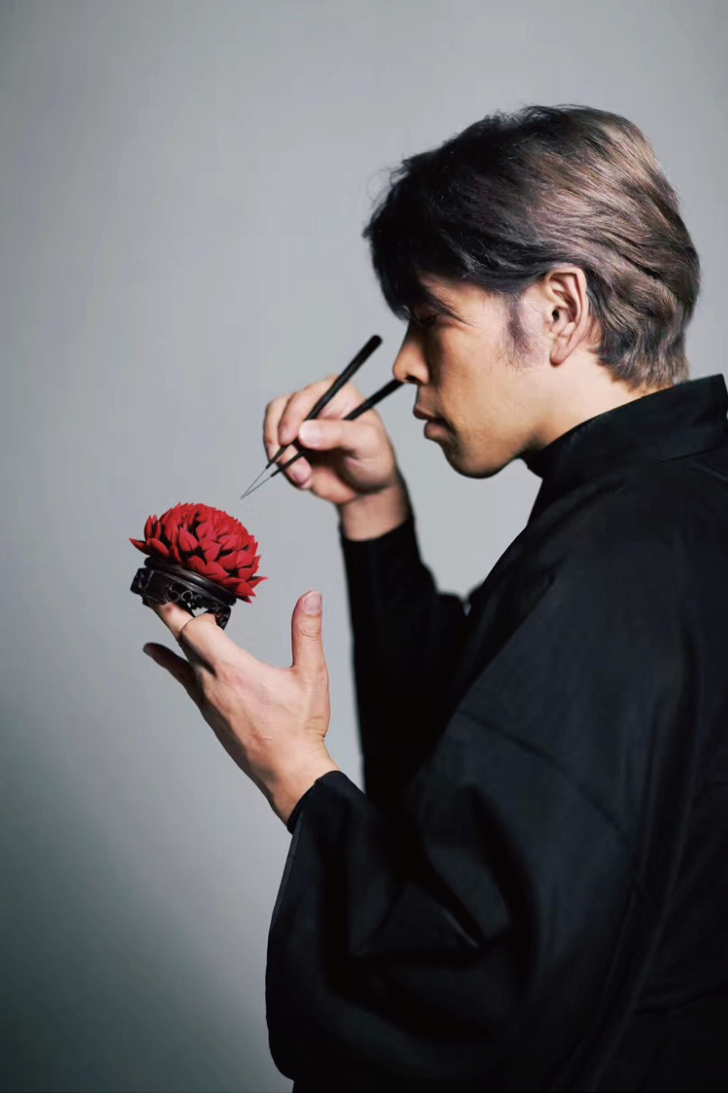 Portrait of wagashi master Junichi Mitsubori crafting a red nerikiri flower with precision tweezers.