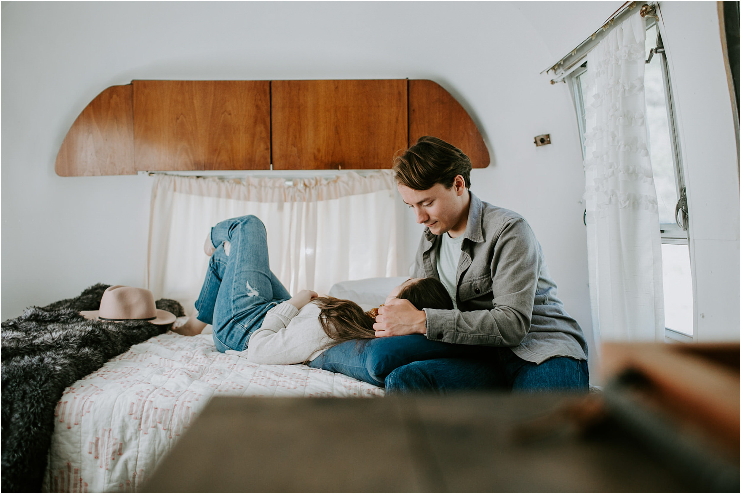 Couple lying on bed in airstream trailer, he is stroking her hair as she lies in his lap.