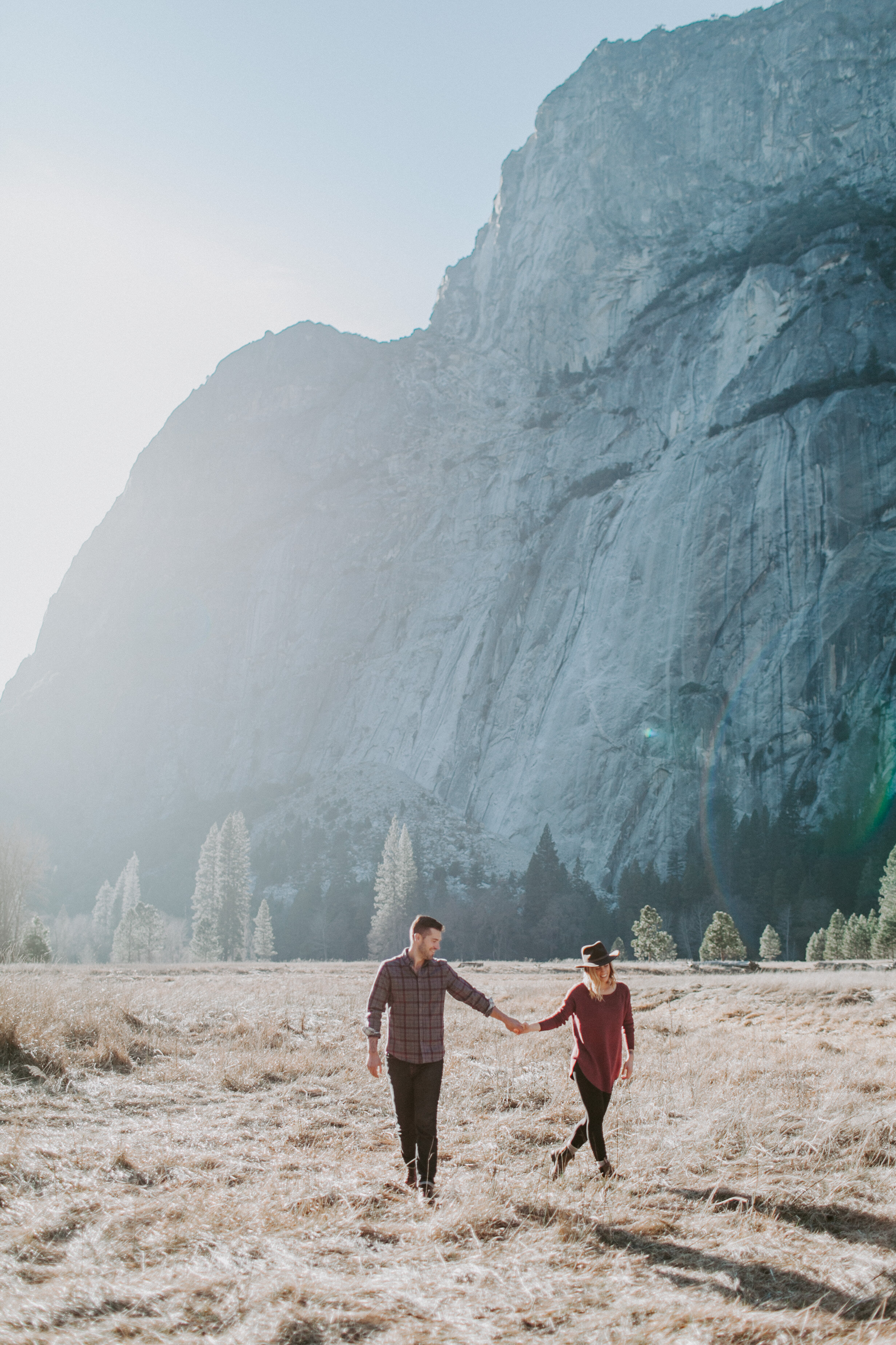  A couple walks in Yosemite Valley holding hands with the sun shining on their backs. 