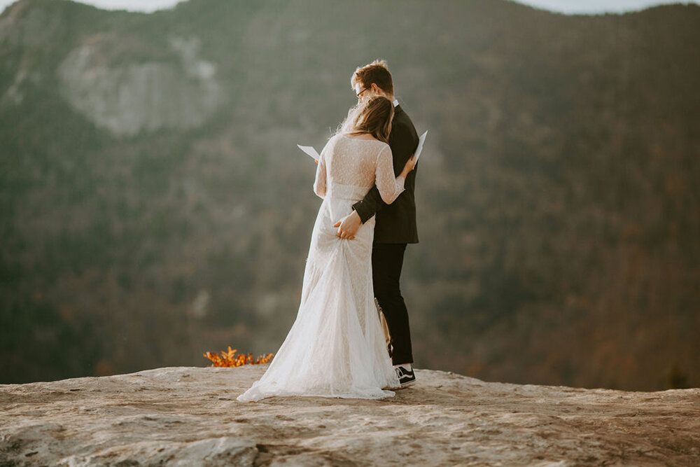 Bride and groom on a mountain for their elopement, exchanging vows and hugging.
