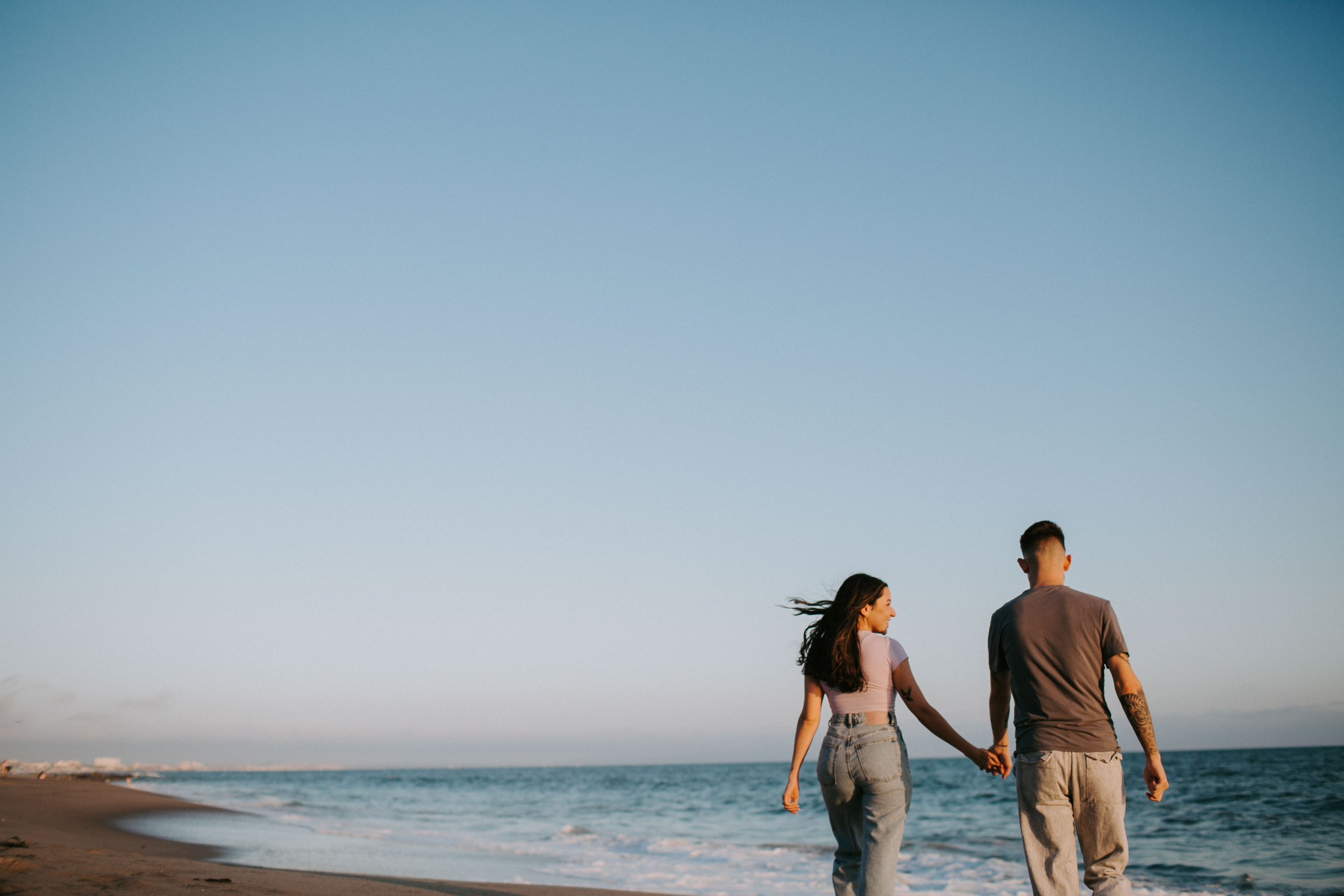  A couple stands on the beach in California holding hands walking towards the water. 