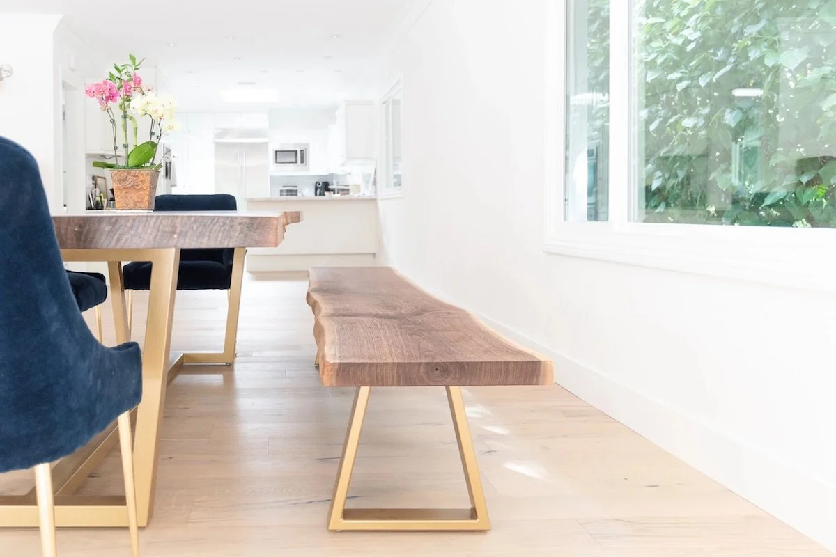 Live edge walnut dining table with matching bench in a contemporary kitchen, featuring custom brass legs and rich wood grain