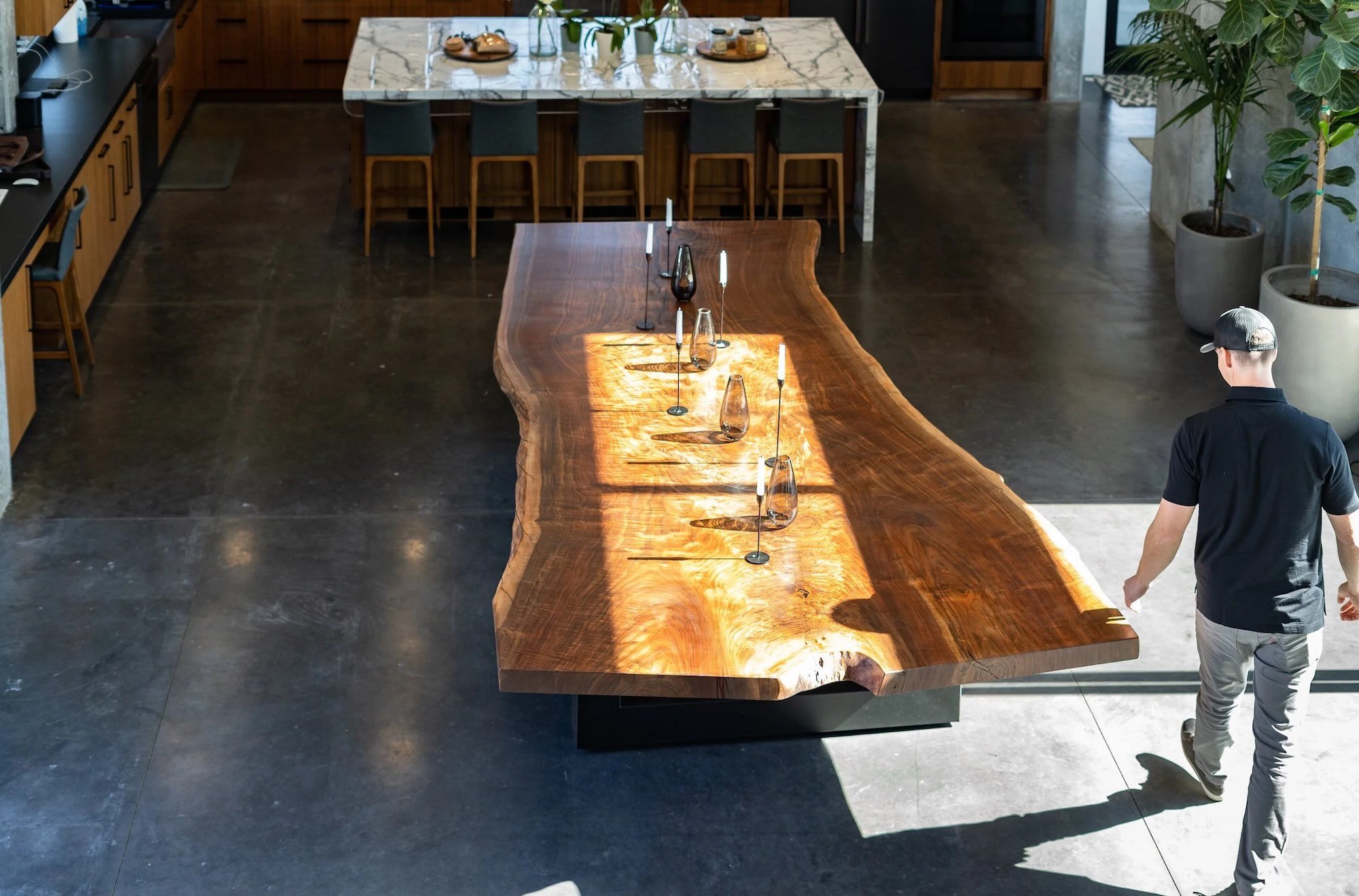Kristopher Kirkpatrick walking beside his handcrafted custom live edge dining table made from premium reclaimed walnut in a modern open-concept kitchen in San Diego