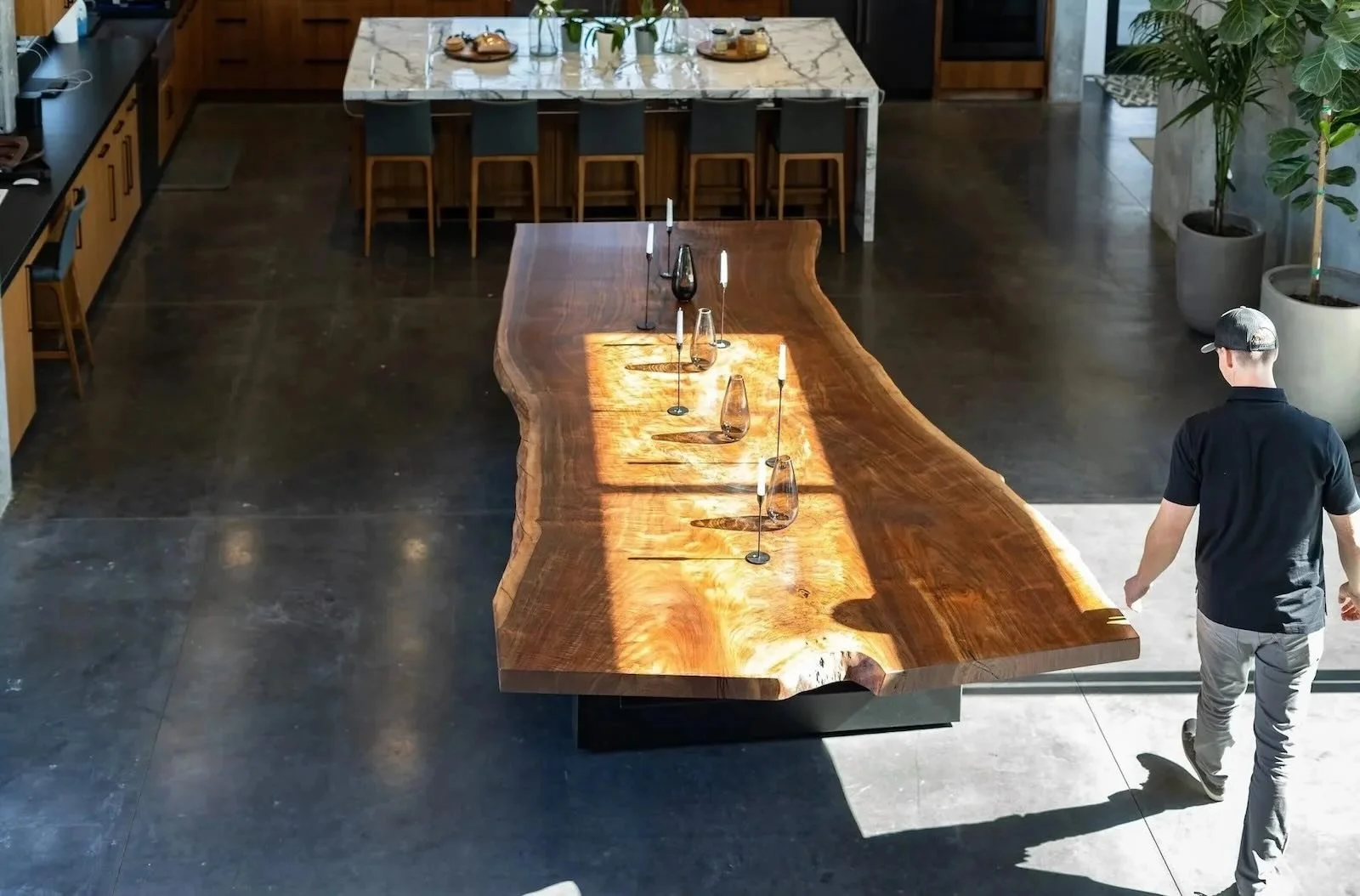 Kristopher Kirkpatrick walking beside his handcrafted custom live edge dining table made from premium reclaimed walnut in a modern open-concept kitchen in San Diego