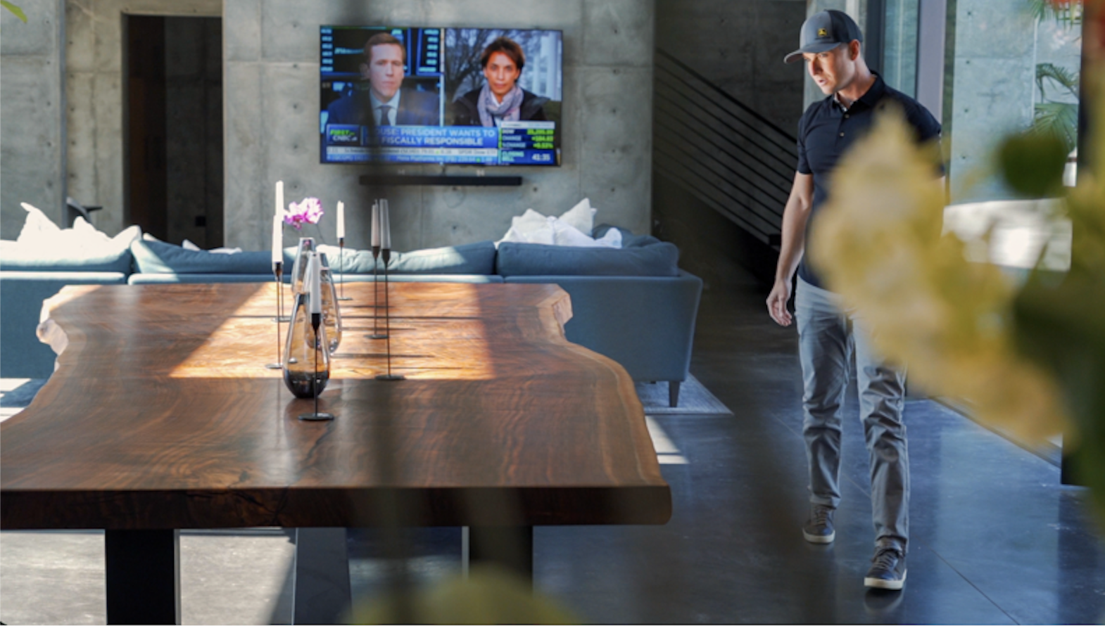 Kristopher Kirkpatrick walking past a large custom live edge dining table in a modern San Diego home, showcasing his handcrafted Claro Walnut furniture with dramatic natural grain and live edges
