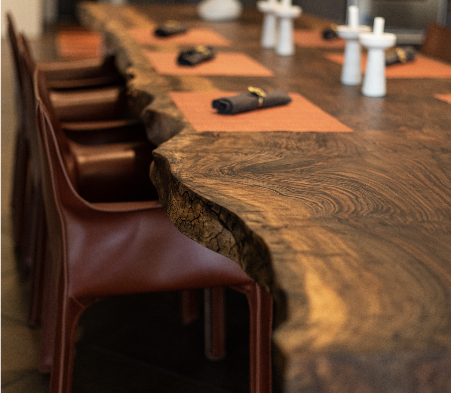 Close-up of rich Bastogne Walnut live edge dining table top showing dramatic natural grain, live edge detail, and durable hardwax oil finish with leather chair in foreground