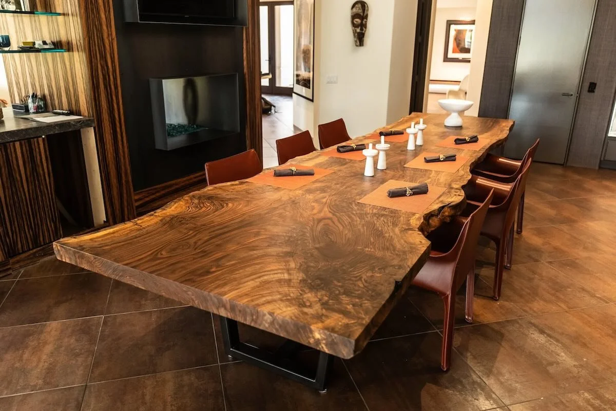 Bastogne walnut live edge dining table with dramatic grain and custom steel base in a warm modern dining room with fireplace