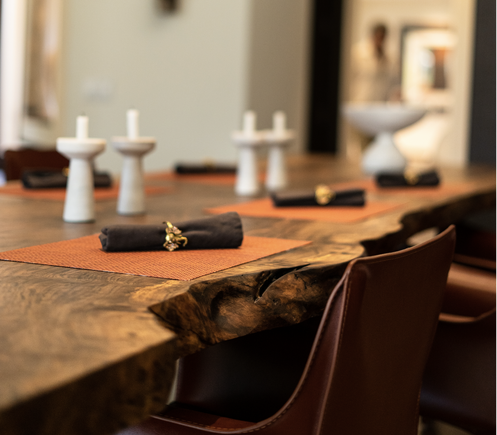 Close-up of live edge Bastogne Walnut dining table with rich natural grain, live edge detail, and premium hardwax oil finish, showing set placemat and leather chair