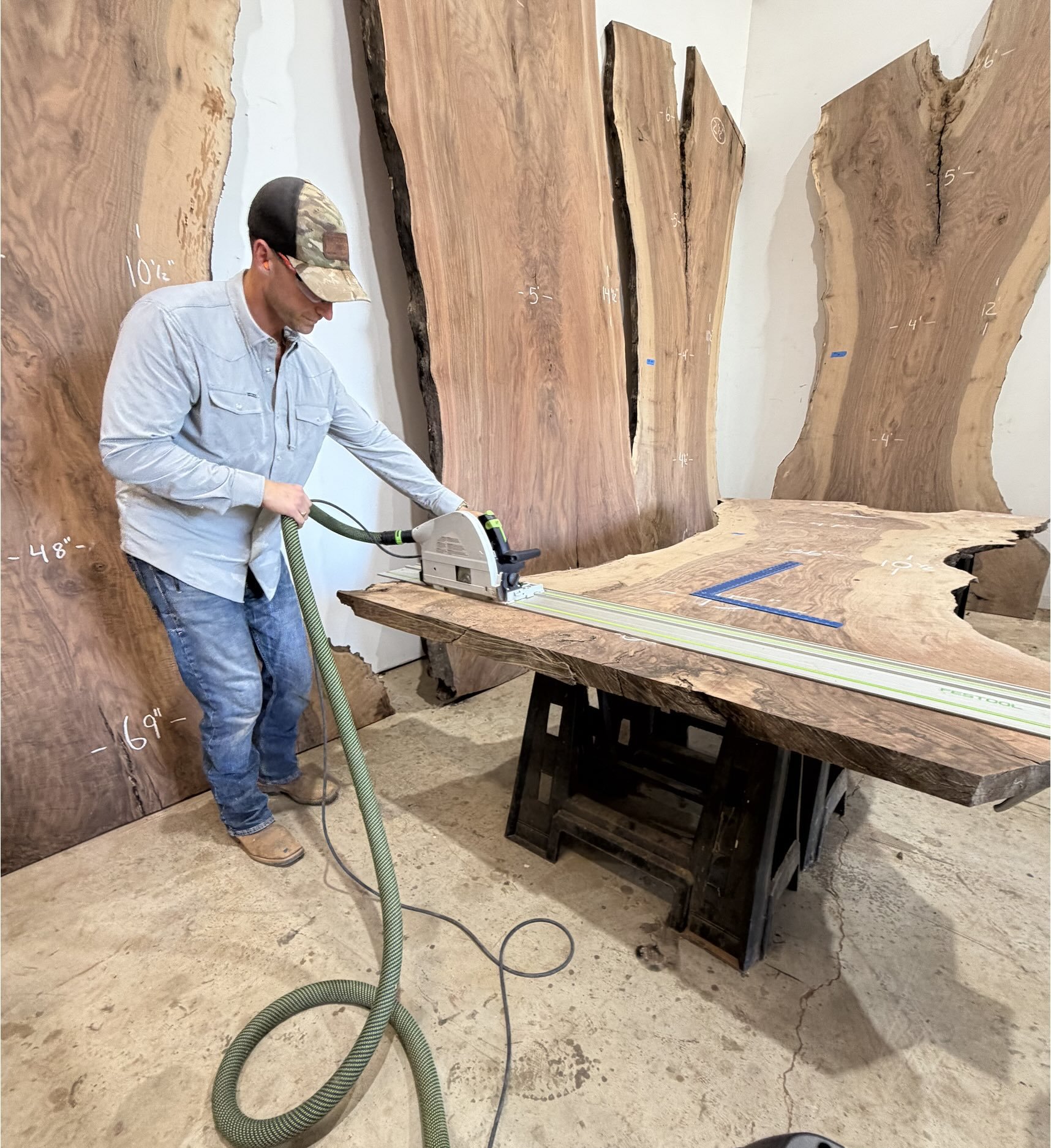 Kristopher Kirkpatrick cutting a large live edge walnut slab with a track saw, surrounded by premium hardwood slabs
