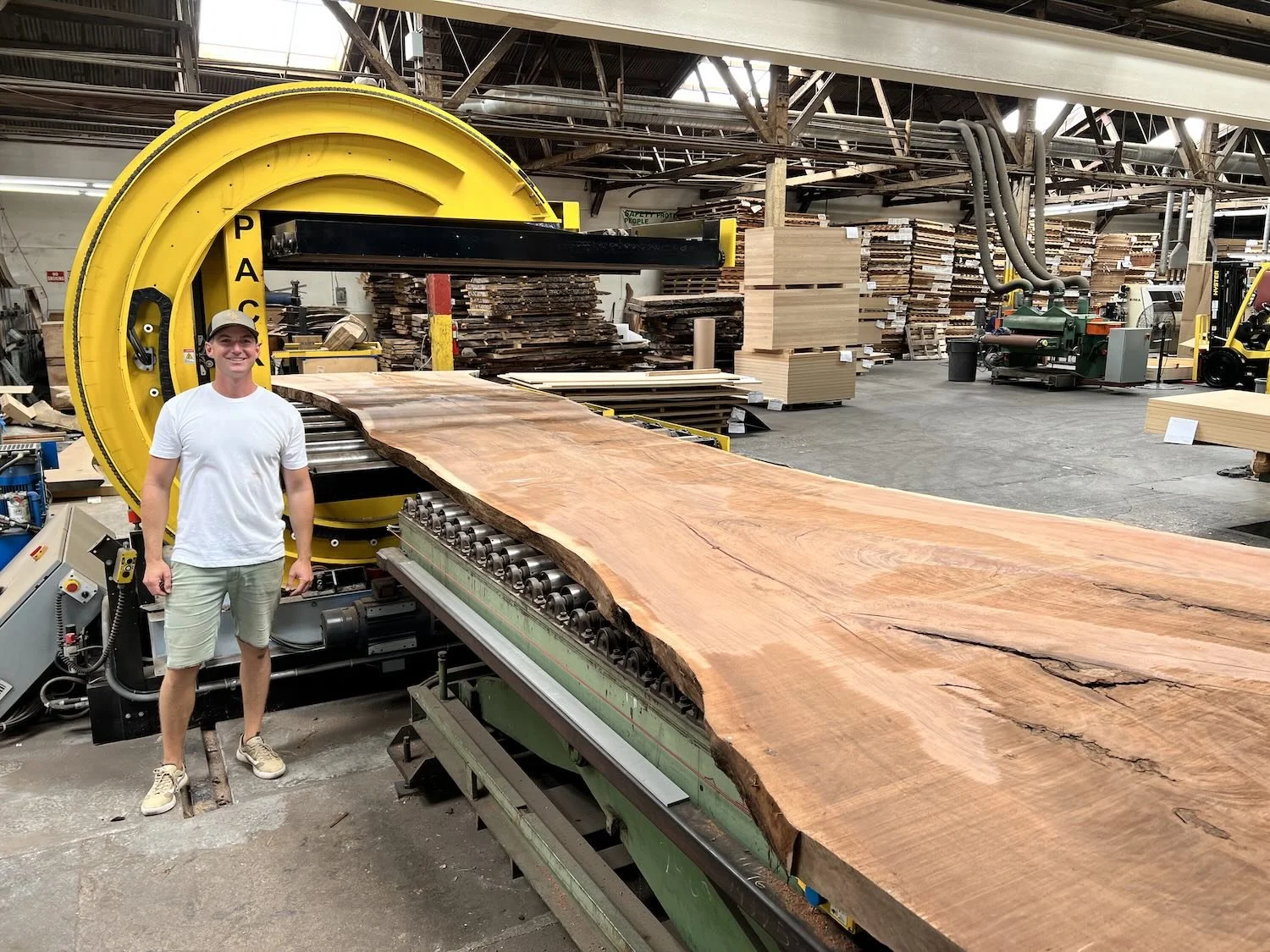 Kristopher Kirkpatrick standing next to a massive live edge Claro walnut slab on the industrial flattener in his San Diego workshop