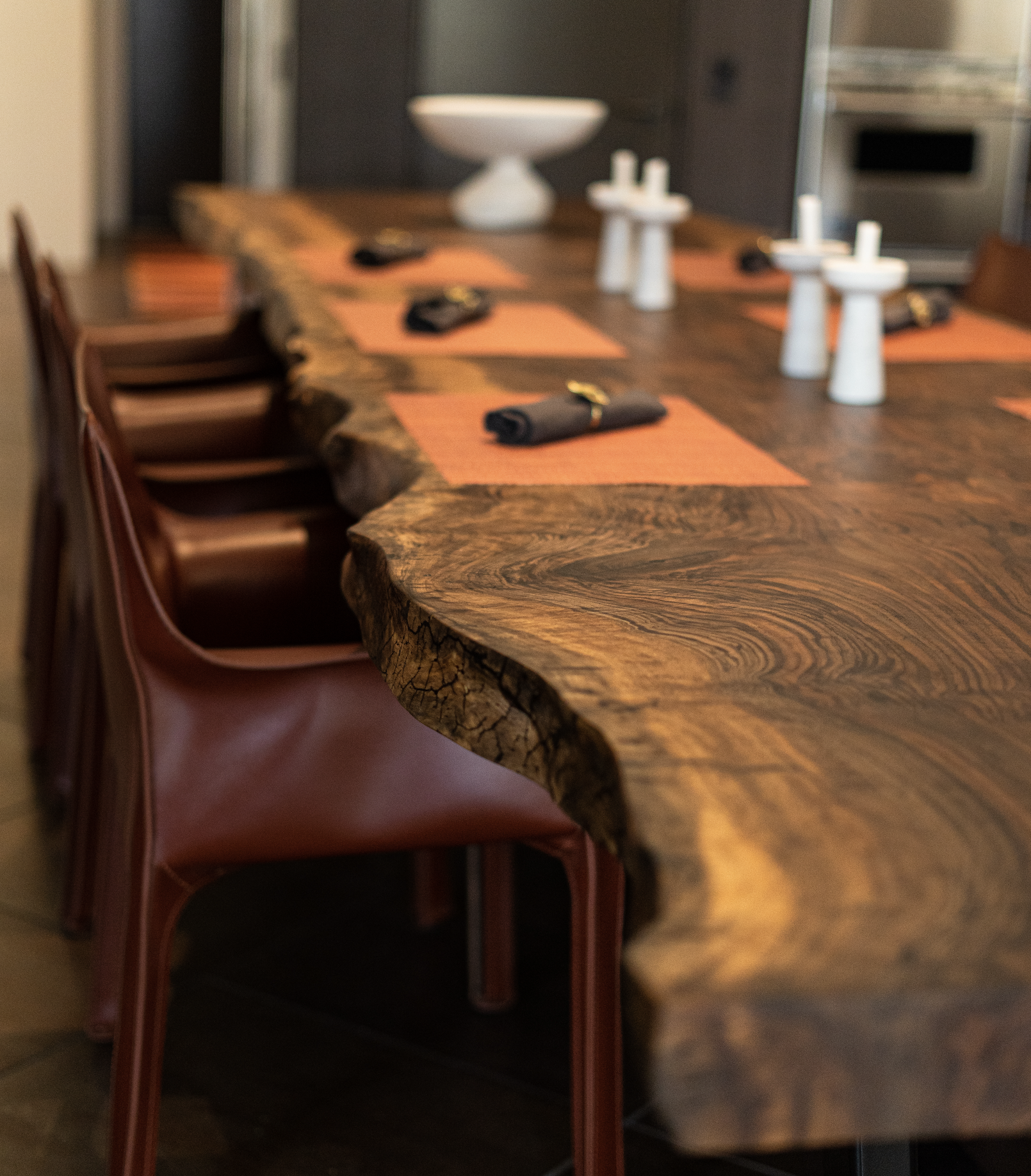 Close-up of rich Bastogne Walnut live edge dining table top showing dramatic natural grain, live edge detail, and durable hardwax oil finish with leather chair in foreground