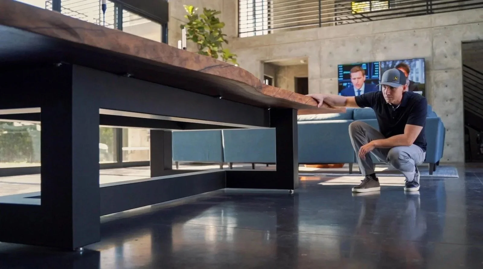 Kristopher Kirkpatrick crouching to inspect the solid black steel base and thick live edge walnut top of his handcrafted custom dining table in a modern San Diego home