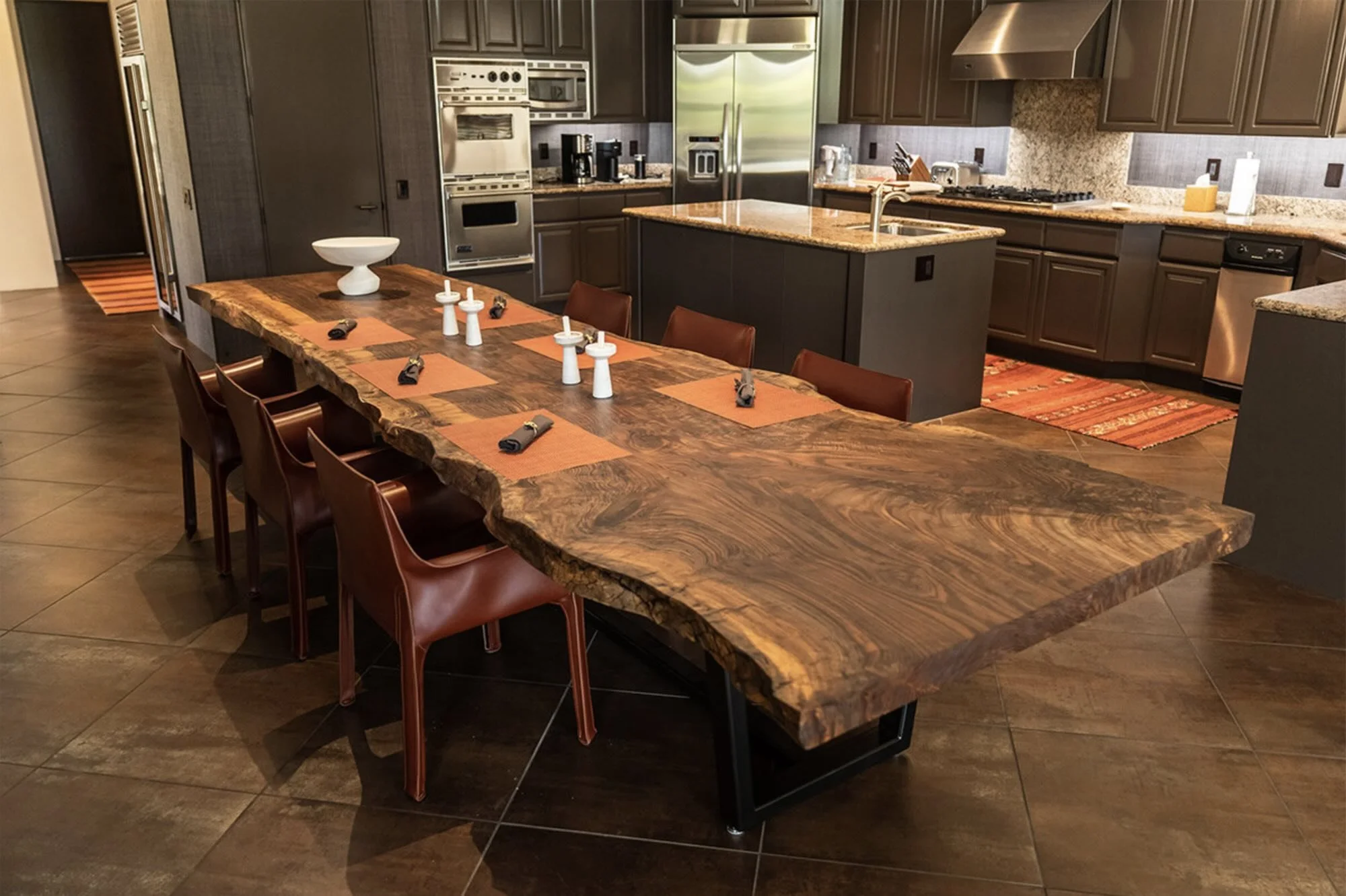 Large live edge Bastogne Walnut dining table with dramatic grain and live edges in a modern open-concept kitchen and dining area with dark cabinetry, handcrafted by Kristopher Kirkpatrick in San Diego