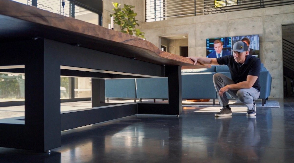 Close-up of historic Claro walnut live edge dining table showing thick slab profile, natural edge detail, and heavy steel base