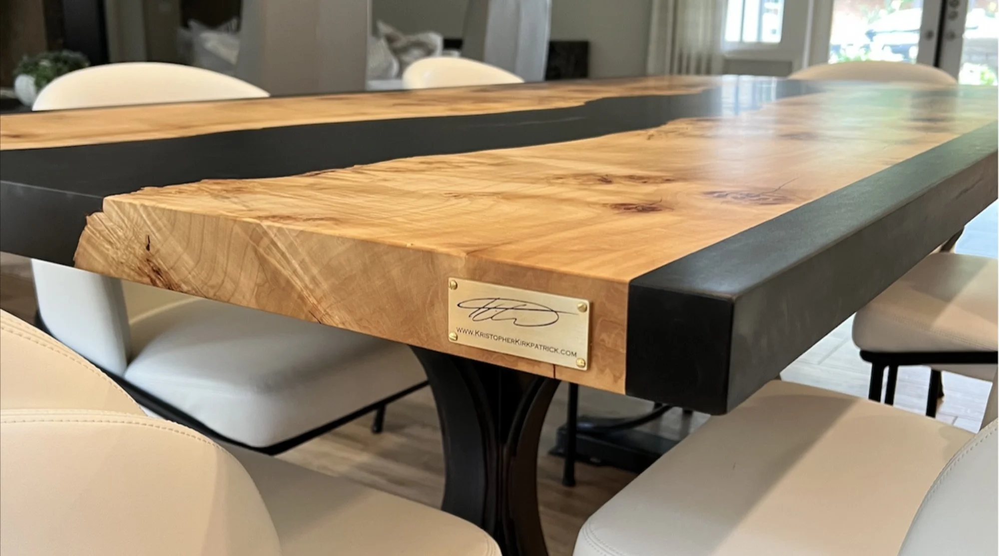 Close-up of custom black epoxy resin river dining table with live edge Burled Maple top, showing rich grain, black resin river, and signature brass plate by Kristopher Kirkpatrick in San Diego