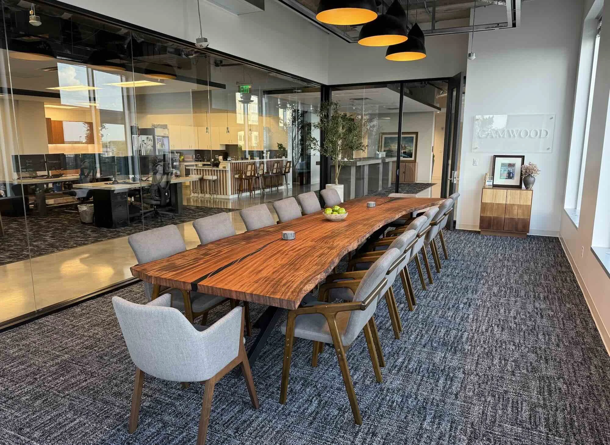 Long live edge Monkey Pod conference table with dramatic natural grain and black steel base in a modern open-plan office with glass walls, custom handcrafted by Kristopher Kirkpatrick in San Diego