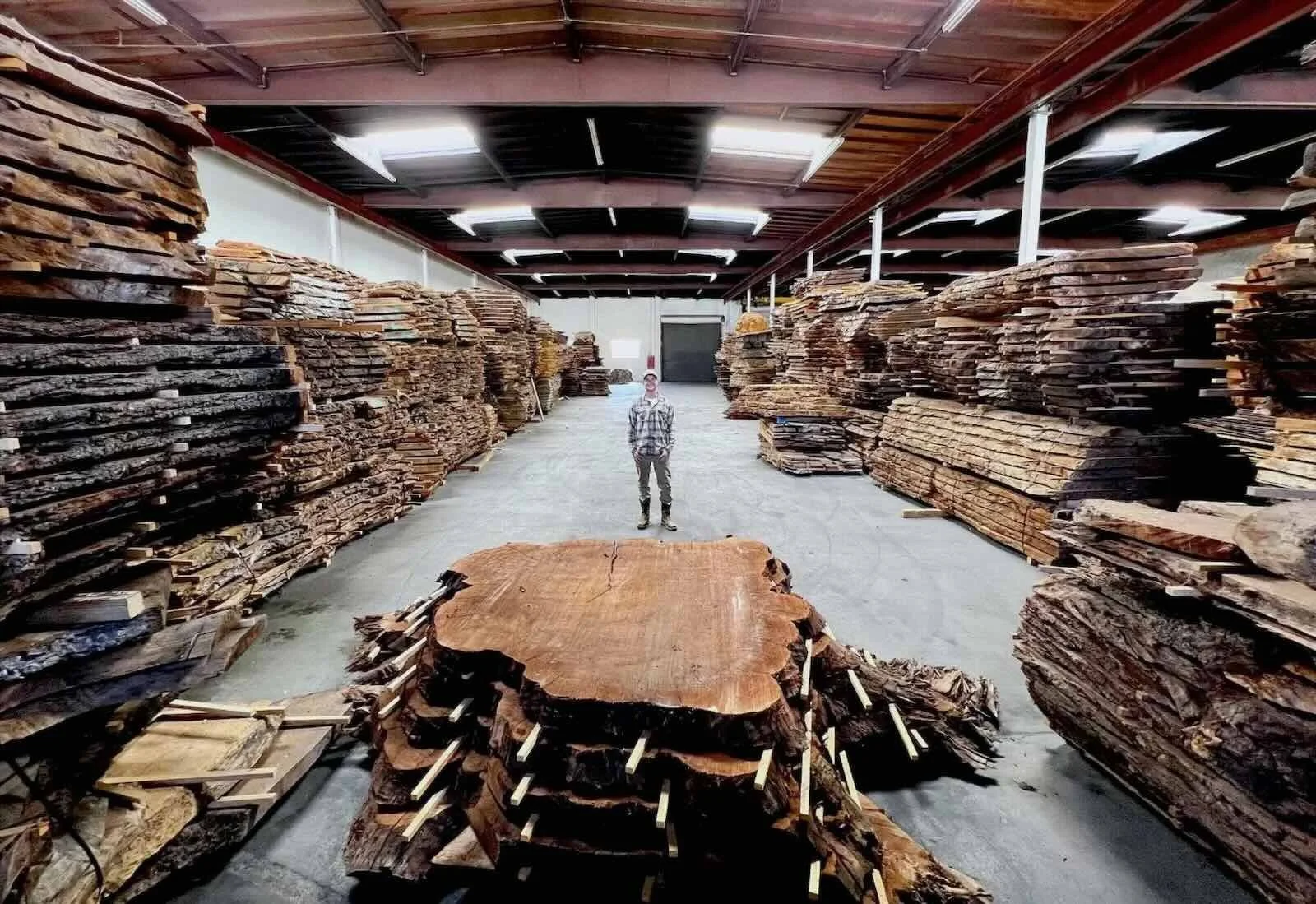 Kristopher Kirkpatrick standing in his San Diego wood shop surrounded by thousands of hand-selected premium reclaimed live edge timber slabs and a massive Claro walnut round