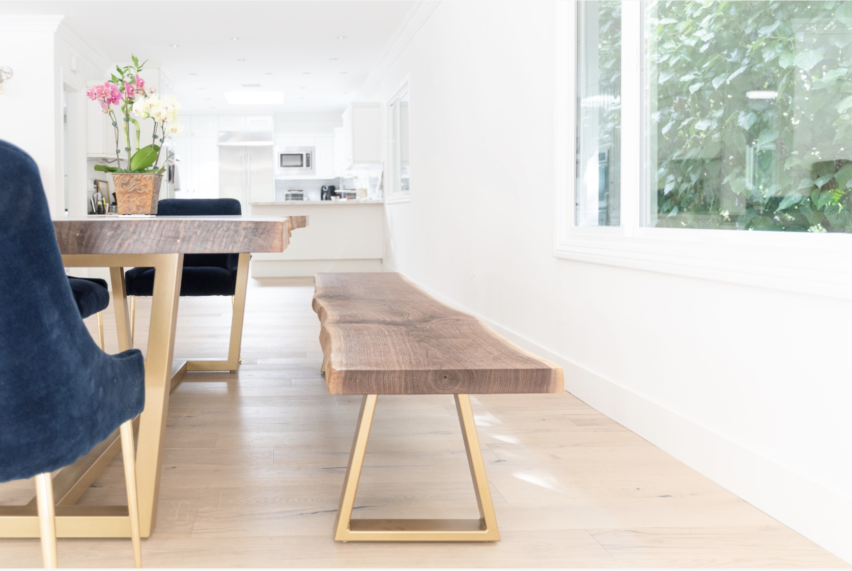 Matching custom live edge Claro walnut bench with brushed gold steel base beside an 8-foot single slab walnut dining table in a modern California home.