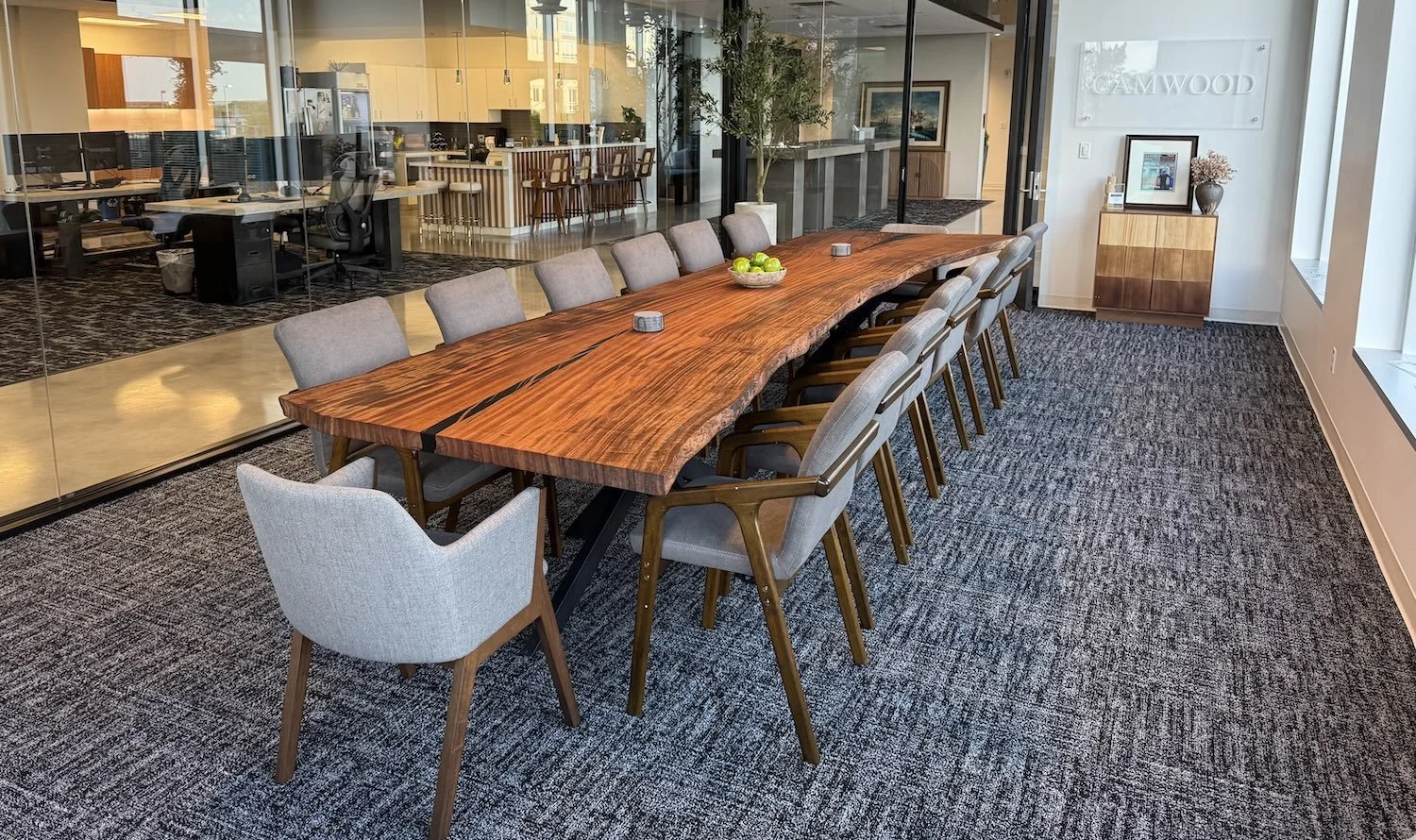 Large single-slab Monkey Pod live edge conference table handcrafted by Kristopher Kirkpatrick, installed in a modern open-plan office with glass walls in San Diego