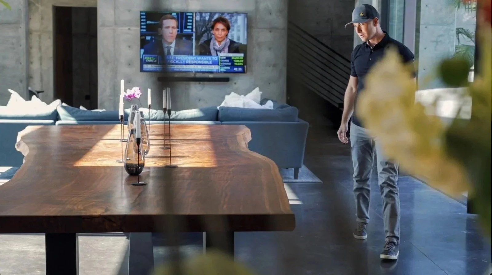 Kristopher Kirkpatrick walking past a large custom live edge dining table in a modern San Diego home, showcasing his handcrafted Claro Walnut furniture with dramatic natural grain and live edges