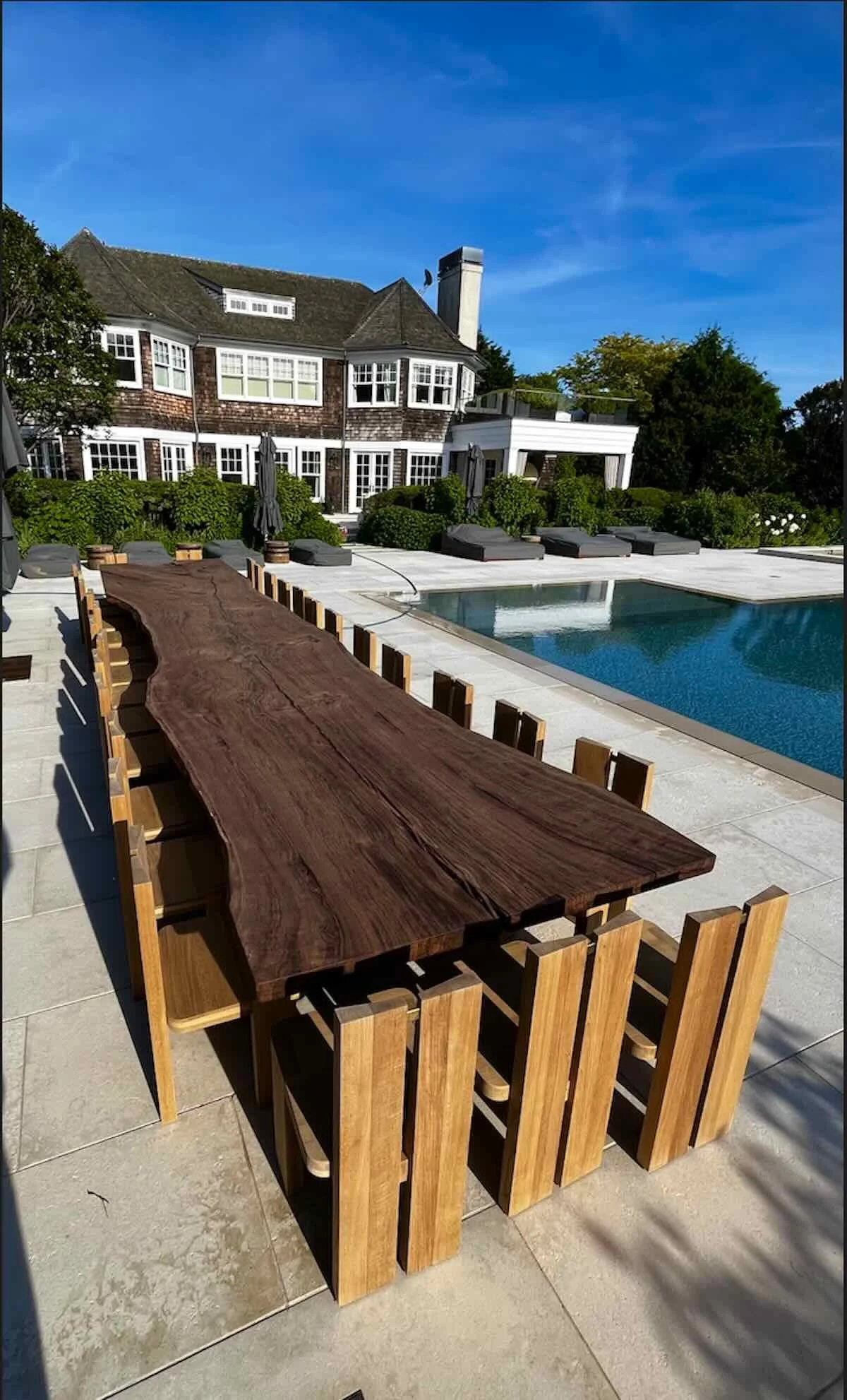 Long outdoor live edge Claro Walnut patio table with wooden chairs beside a swimming pool at a backyard estate