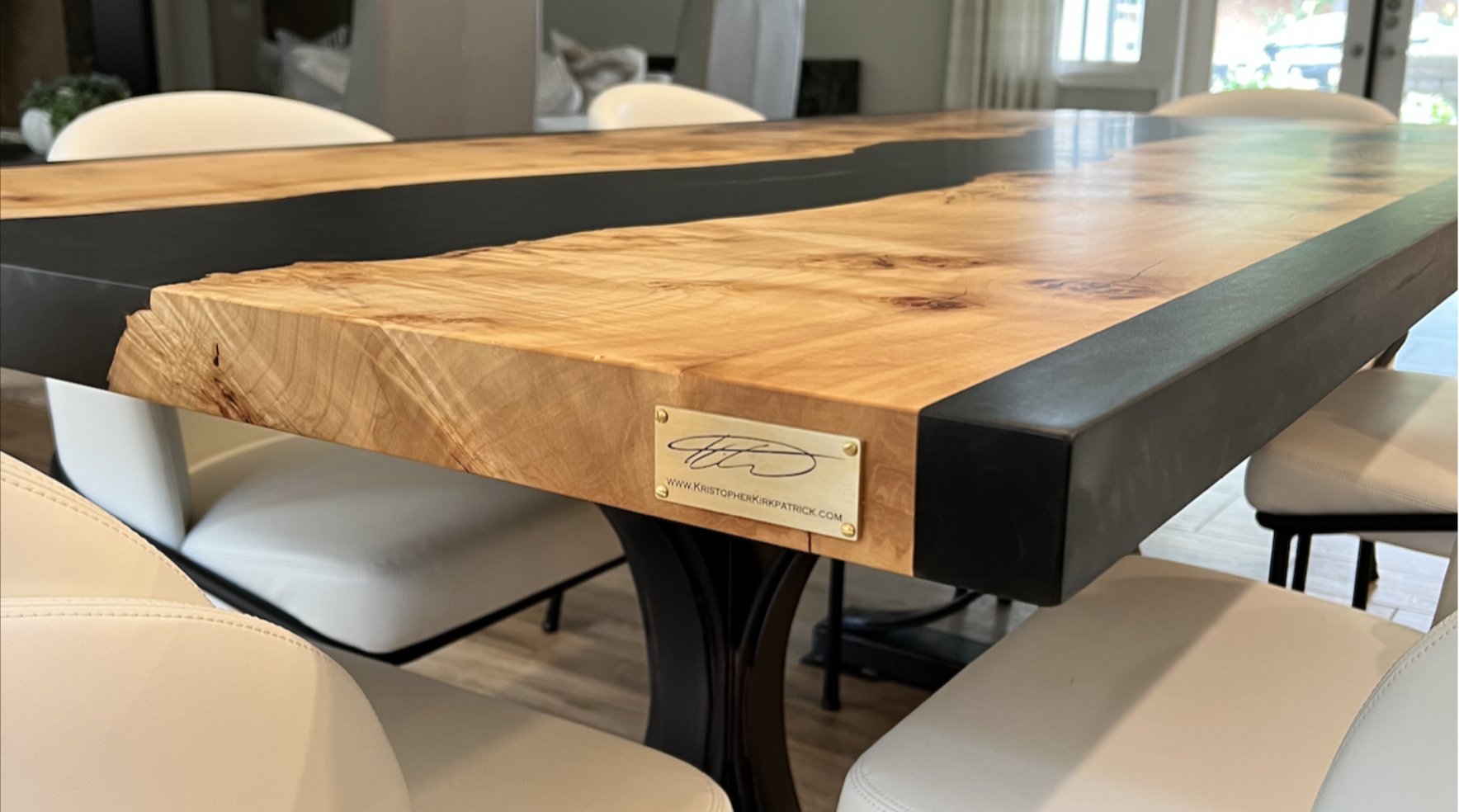 Close-up of custom black epoxy resin river dining table with live edge Burled Maple top, showing rich grain, black resin river, and signature brass plate by Kristopher Kirkpatrick in San Diego