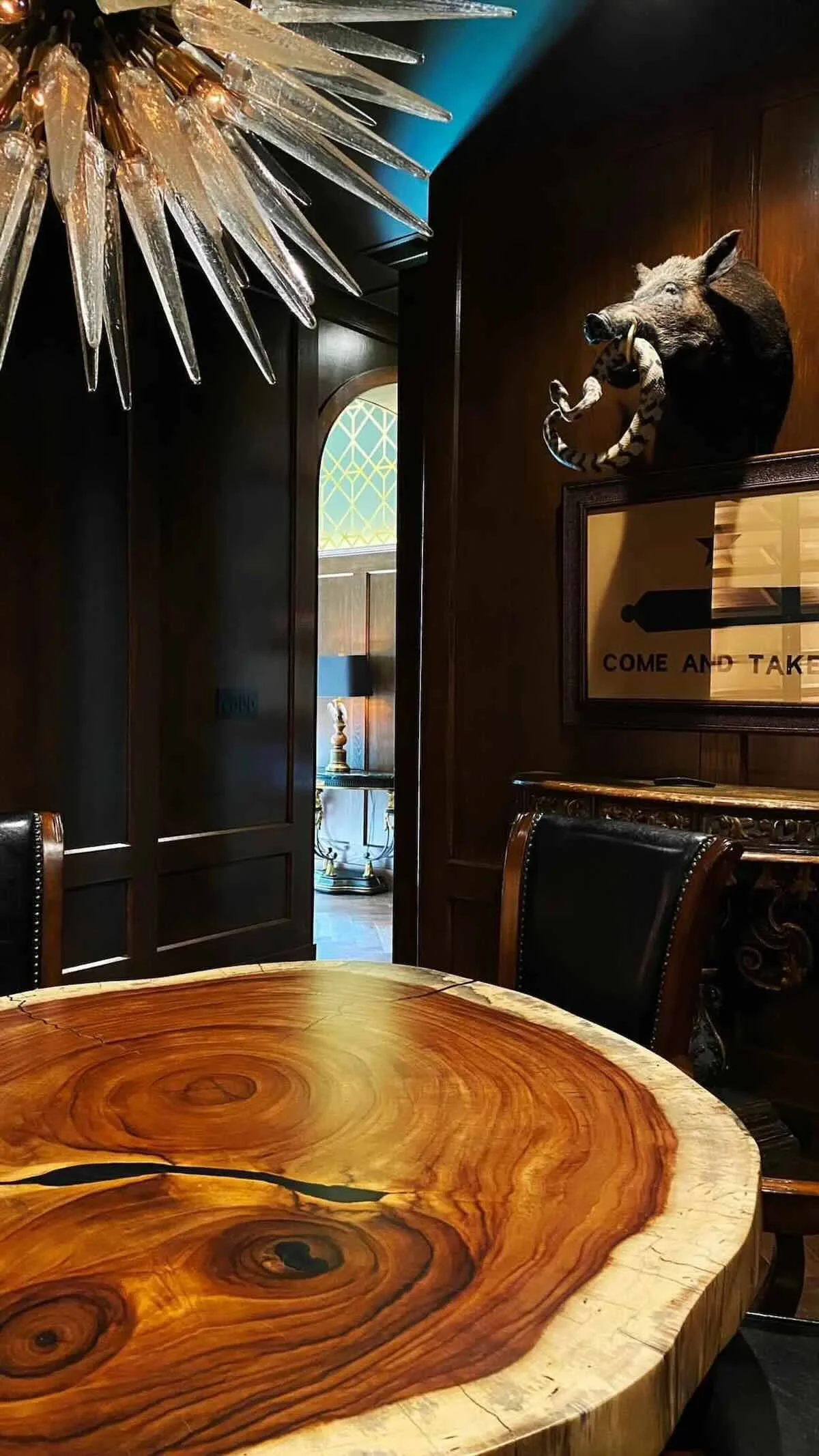 View into exclusive live edge poker table room with dark wood paneling, leather chairs, and custom Acacia slab poker table