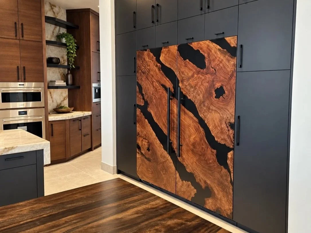Custom Sub-Zero refrigerator door panels handcrafted from richly figured Claro walnut and contrasting black epoxy resin, installed in a luxury kitchen with dark cabinetry.