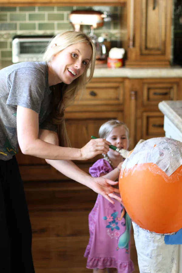 Lily is helping me paint the other side of the balloon. Good big sister. Same process as before. Soak all your strips and place them directly to the balloon then coat again with the glue mixture. You are going to do this three times. Just like you did with the cone. Each layer has to dry 24 hours before starting the next layer. And make sure you overlap your layers onto the cone itself. It should connect. Yup, this is a long process. I told you. Don't I look happy though?